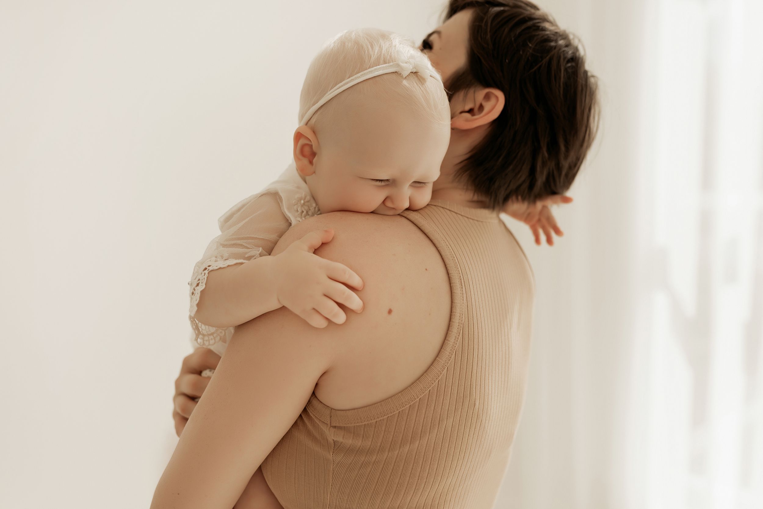 Tender moment captured as parent holds infant against neutral background.