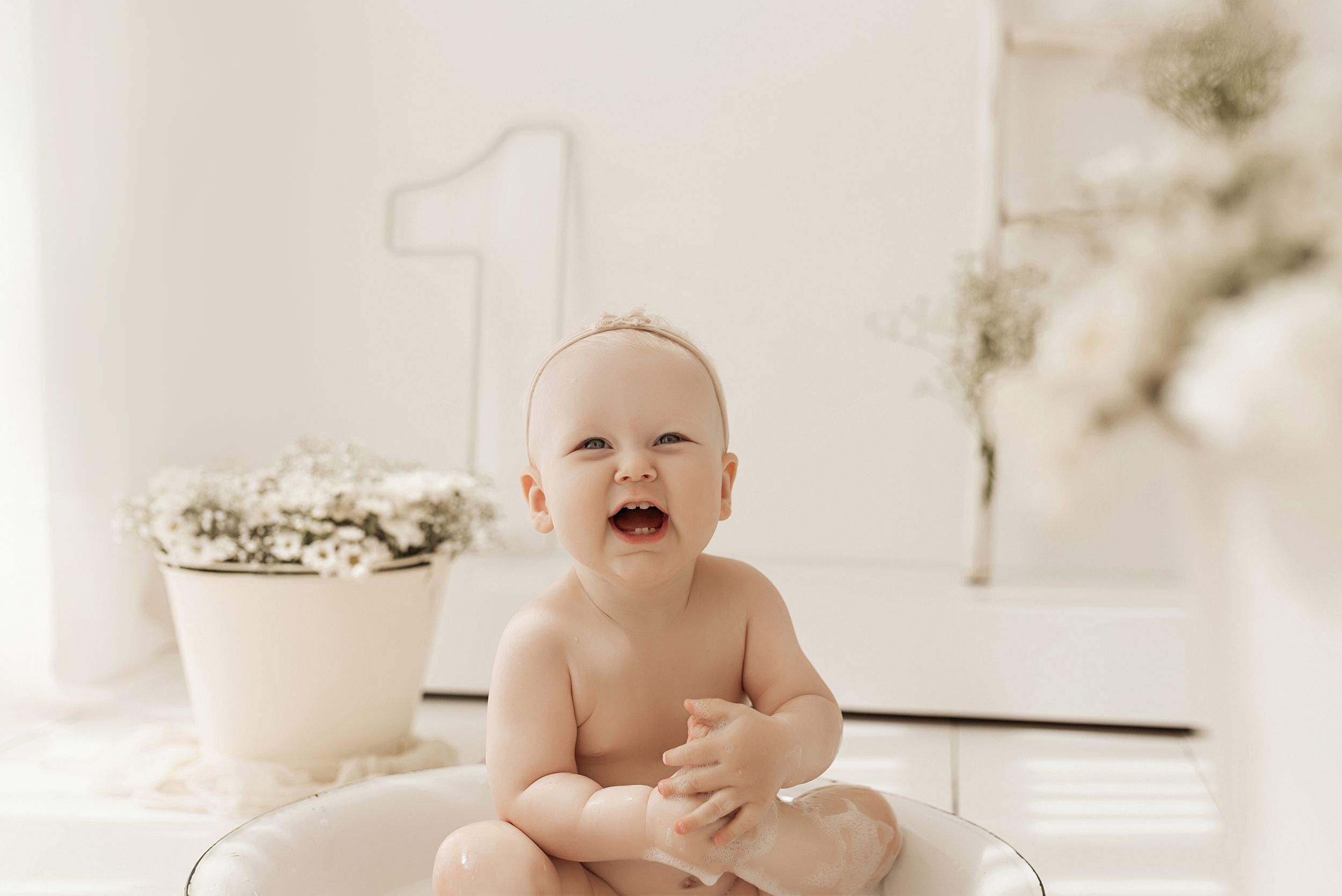 Happy baby sits beside number one decoration during first birthday photoshoot.