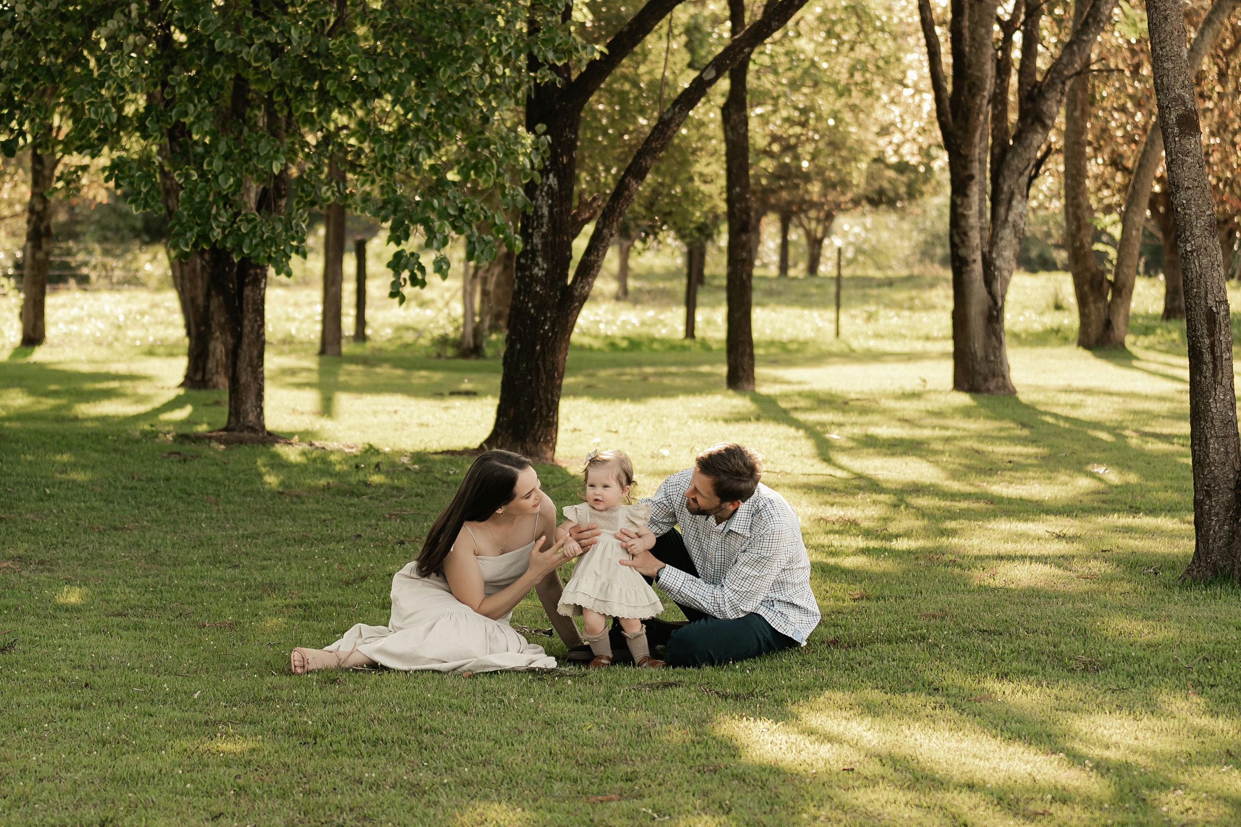 Family relaxing together on grass in a sunlit park setting.