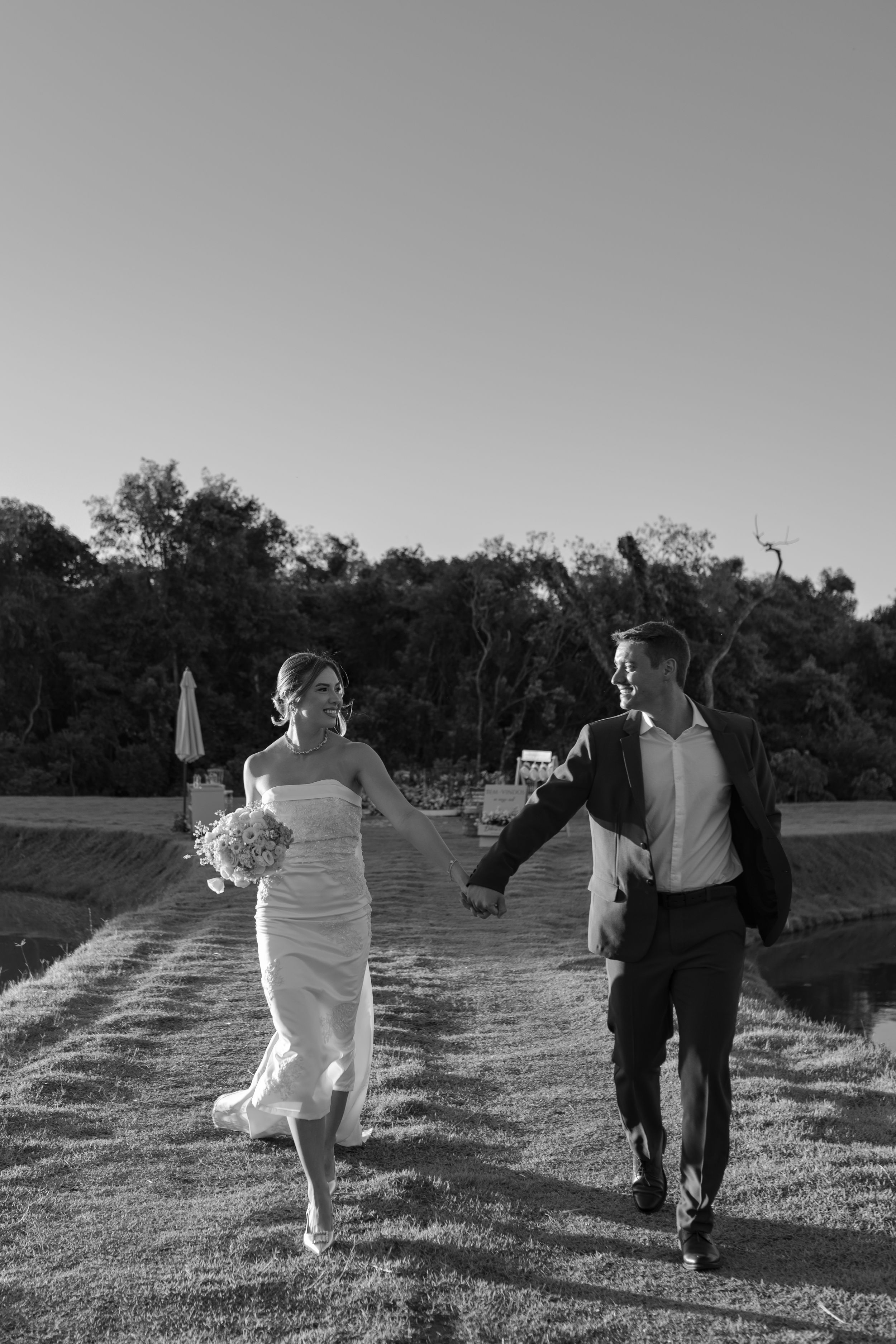 A couple runs joyfully together on a path through nature in black and white photography.