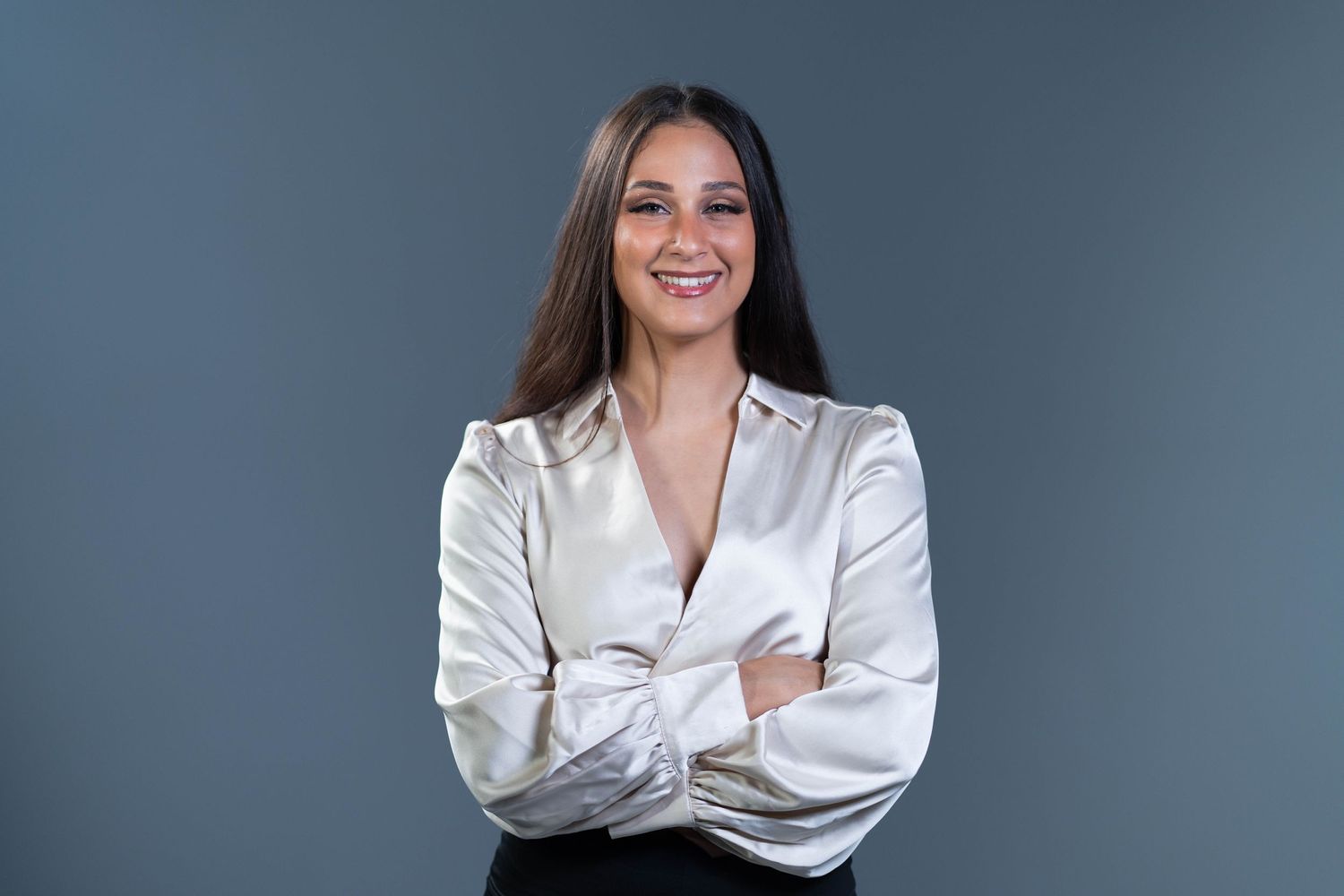 Professional headshot of person in white satin blouse against blue background.