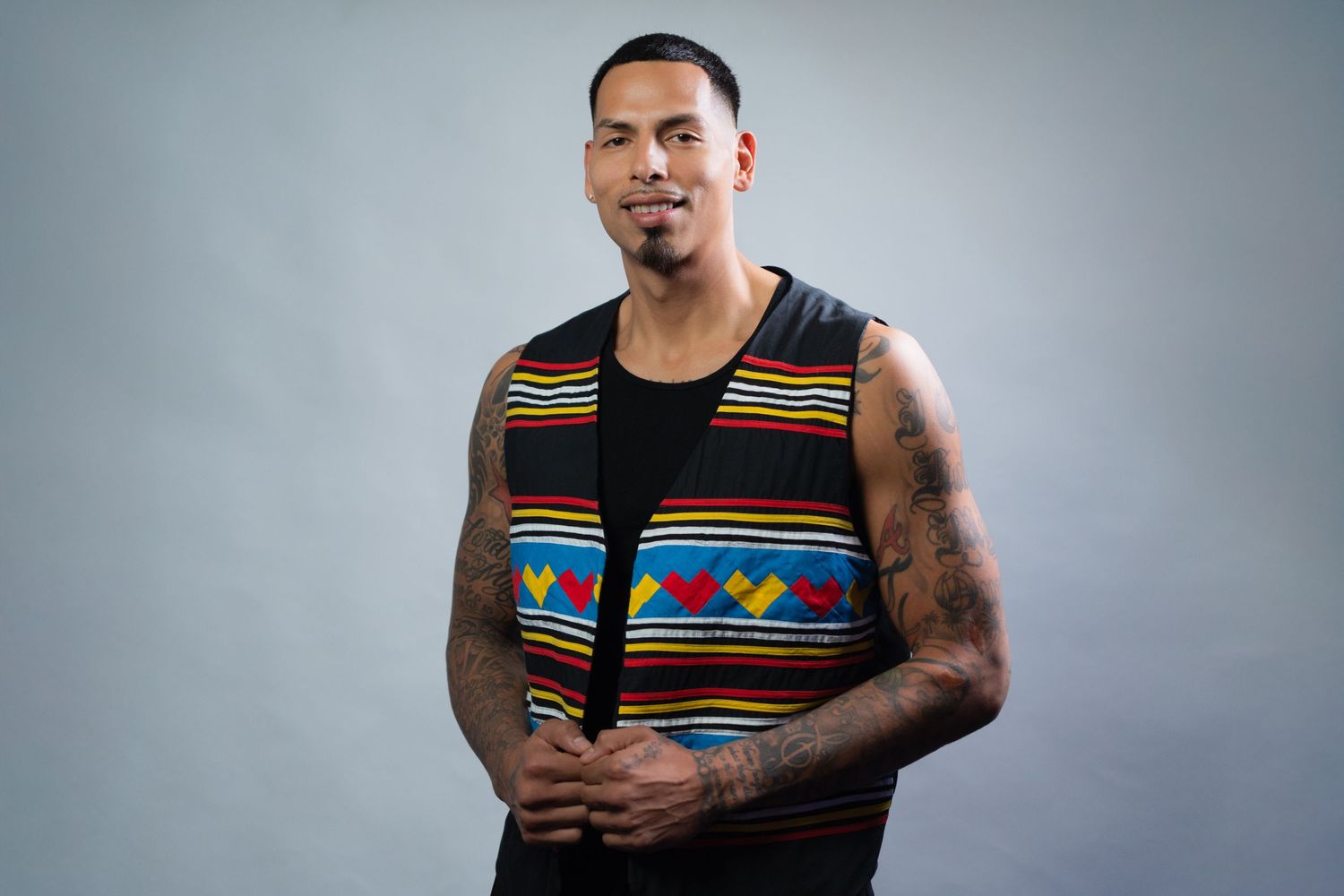 Man wearing traditional patterned vest poses in studio setting for professional headshots