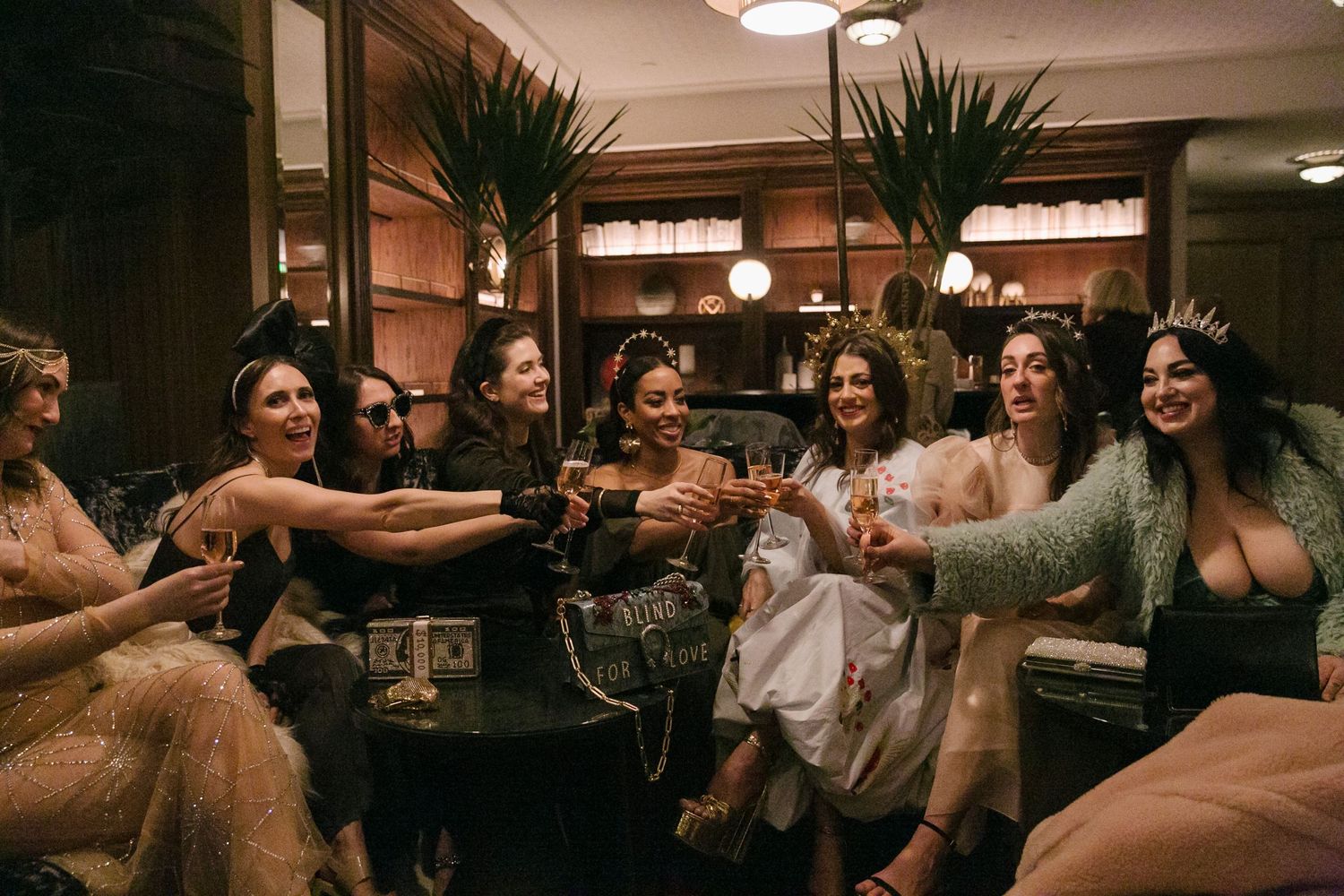 A group of friends toasting and celebrating together in a cozy indoor setting with warm lighting and palm plants.
