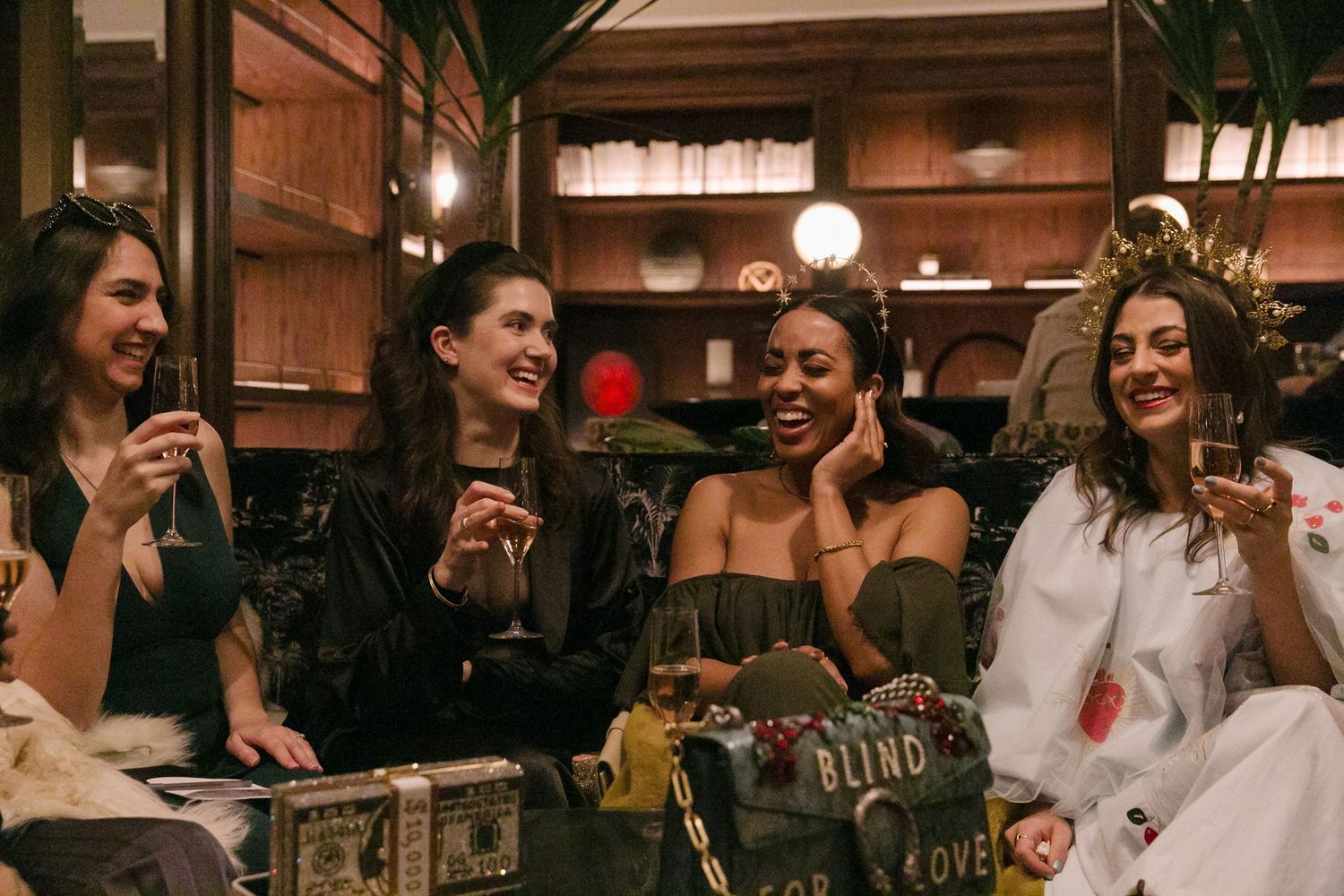 A group of friends enjoying drinks and laughter together at a restaurant with warm wooden decor and ambient lighting.
