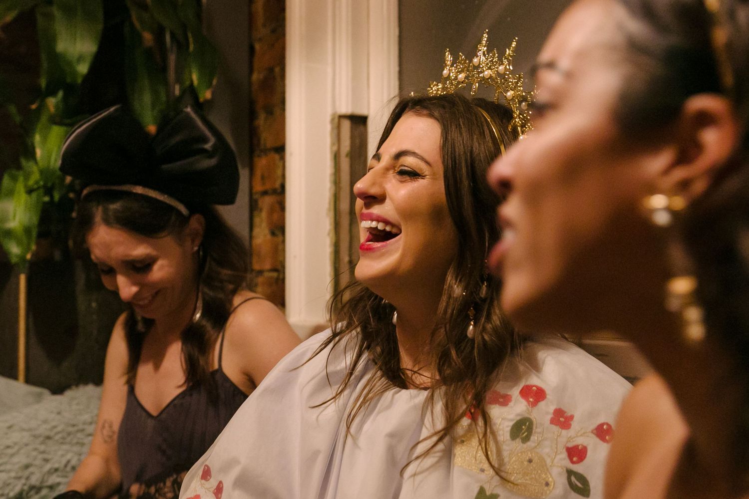 Three people share a joyful moment of laughter at a celebration, with one wearing a delicate crown.