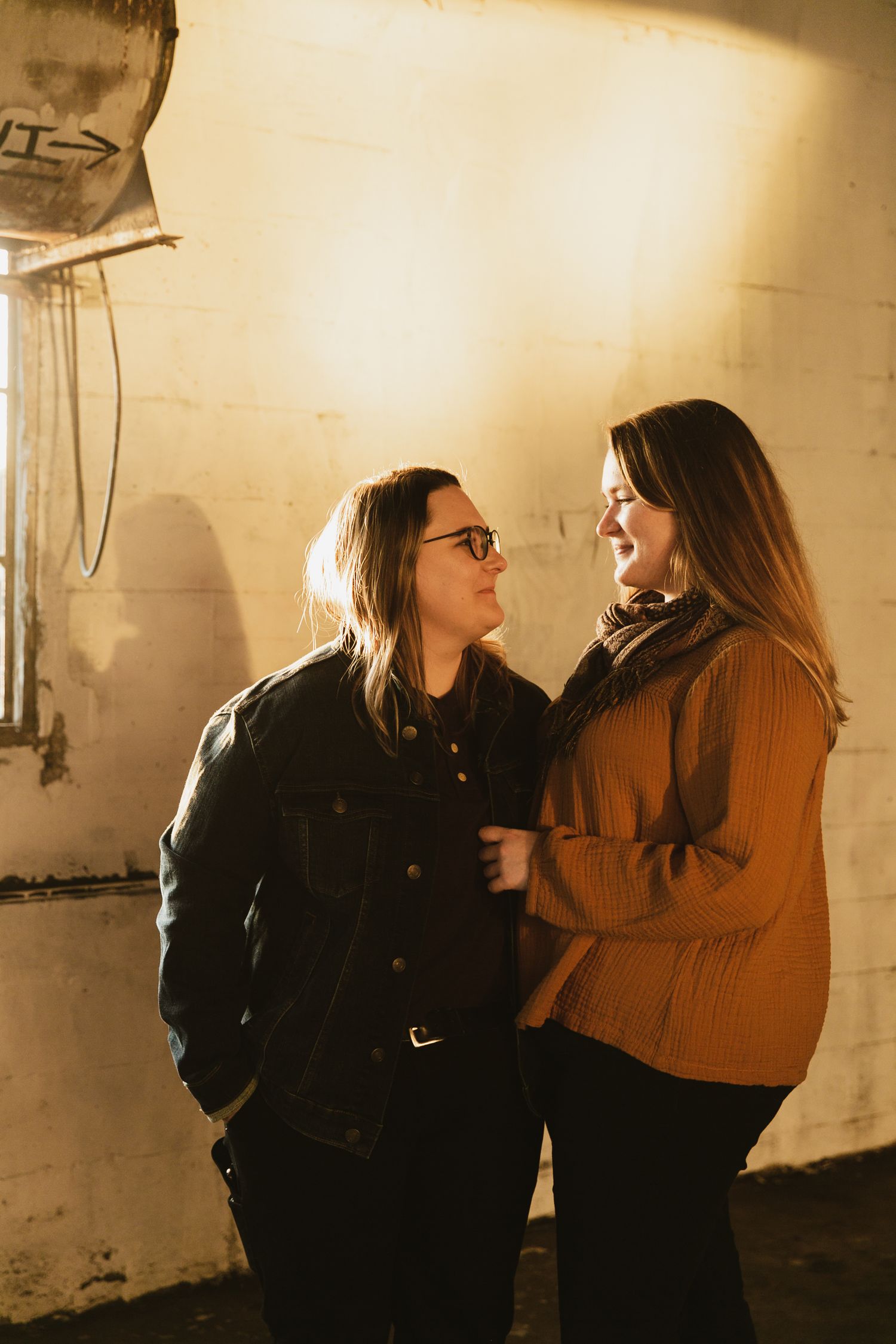 A couple sharing an intimate moment against a cream-colored wall in warm ambient lighting.