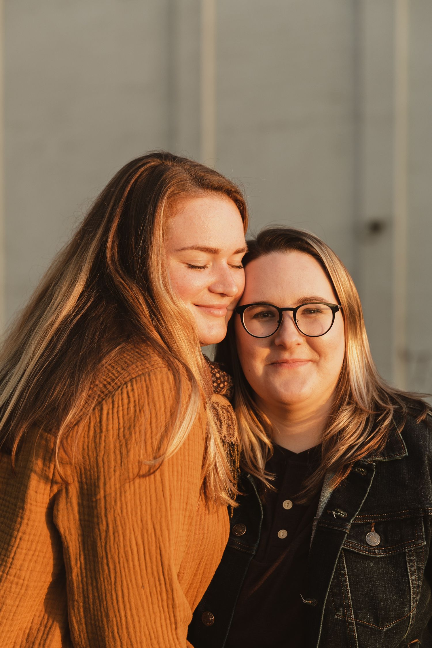 Two people sharing an intimate moment in warm lighting, one wearing a brown sweater and one in a denim jacket.