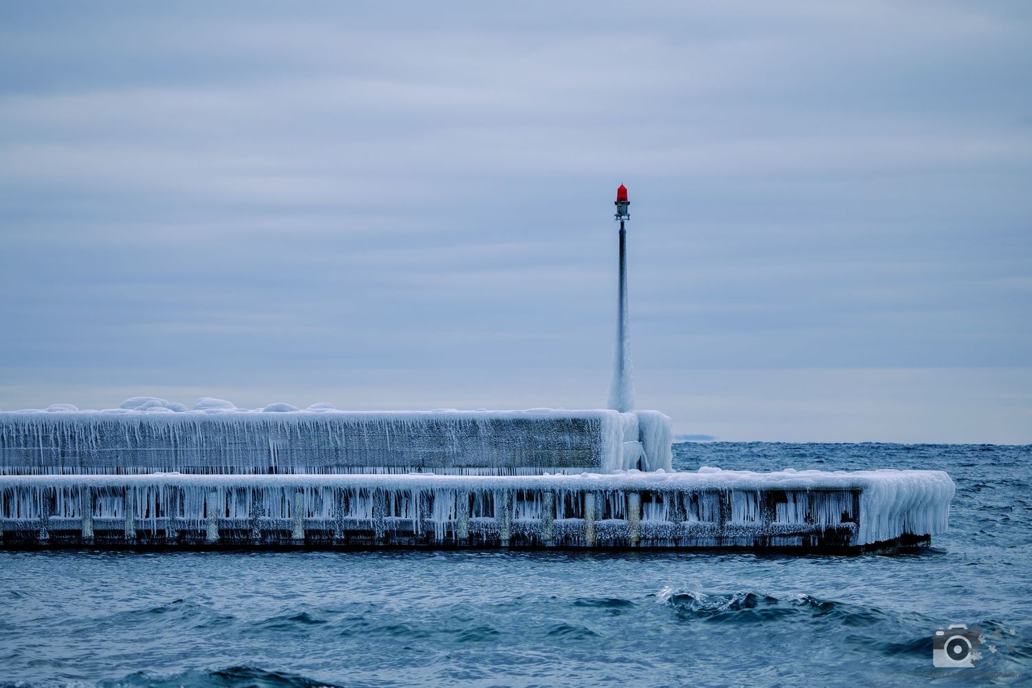 A frozen lighthouse pier covered in ice alongside Lake Superior during winter.