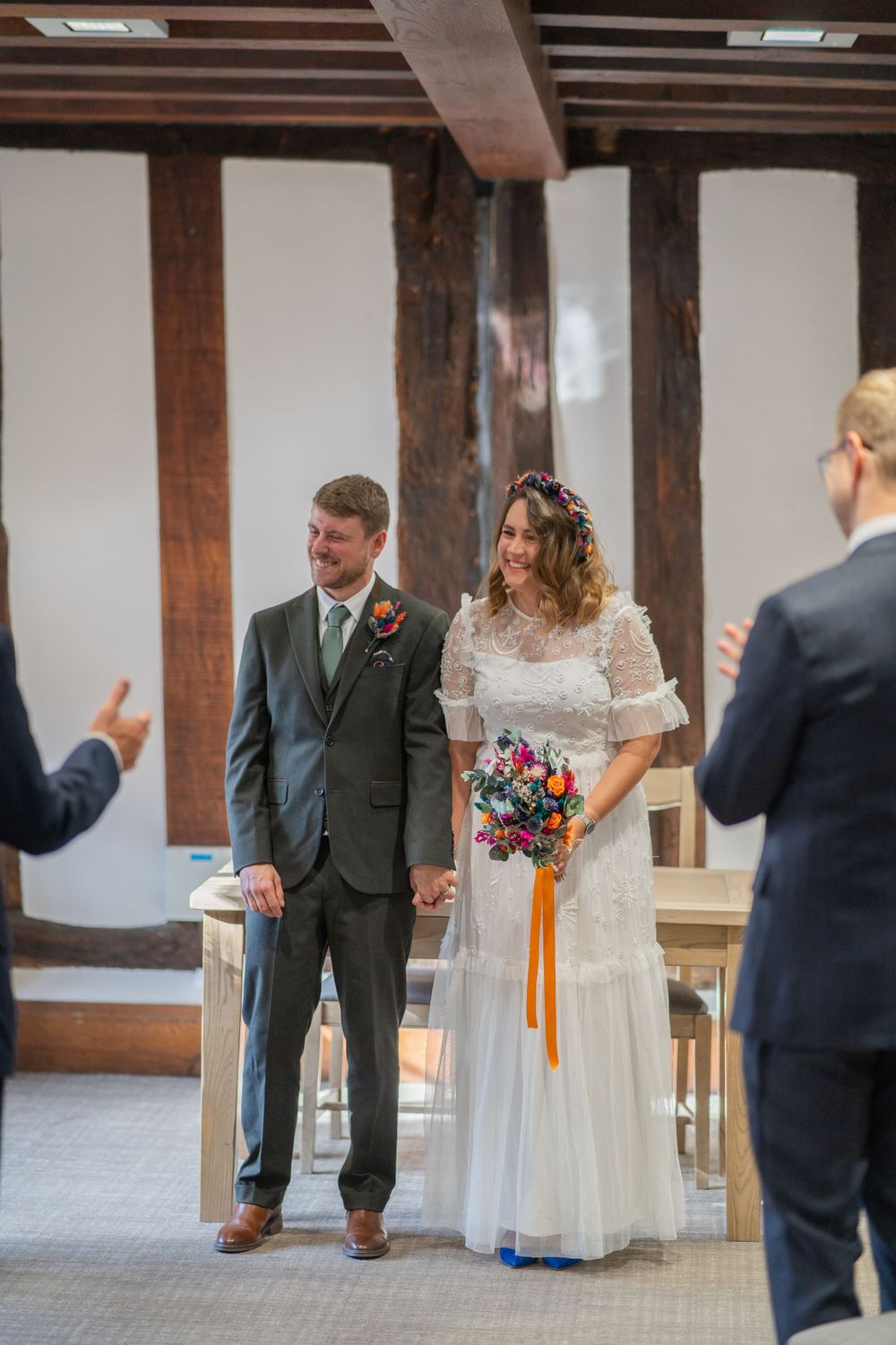 A couple stands together during their wedding ceremony in a rustic venue with exposed wooden beams.