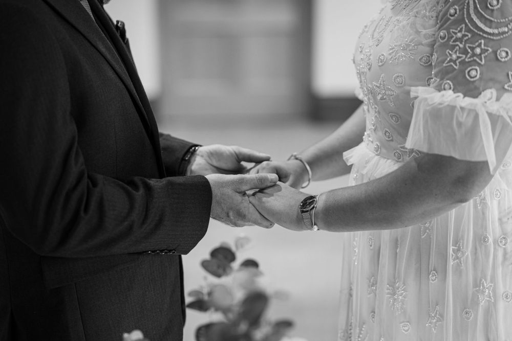 Black and white close-up photo of hands exchanging rings during a wedding ceremony.