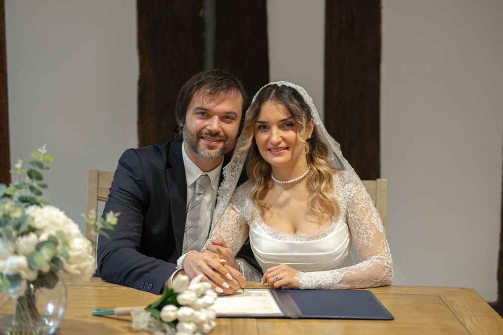 A happy couple shares a joyful moment at their wedding ceremony while seated at a table with flowers.