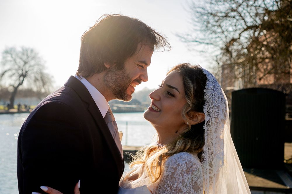 A couple shares a romantic moment in lace wedding attire by a waterfront during golden hour.