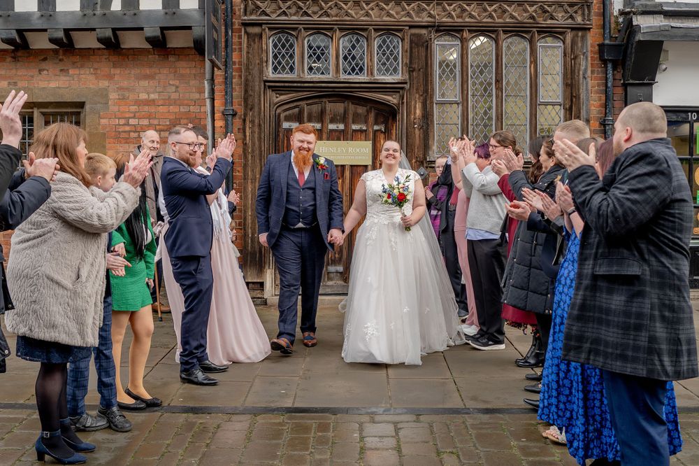Wedding guests line both sides of a historic entrance as newlyweds exit through a grand wooden doorway.