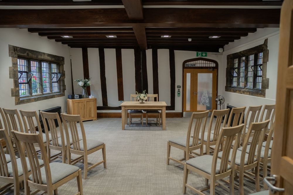 Interior view of a rustic meeting room with wooden chairs arranged in rows and exposed ceiling beams.