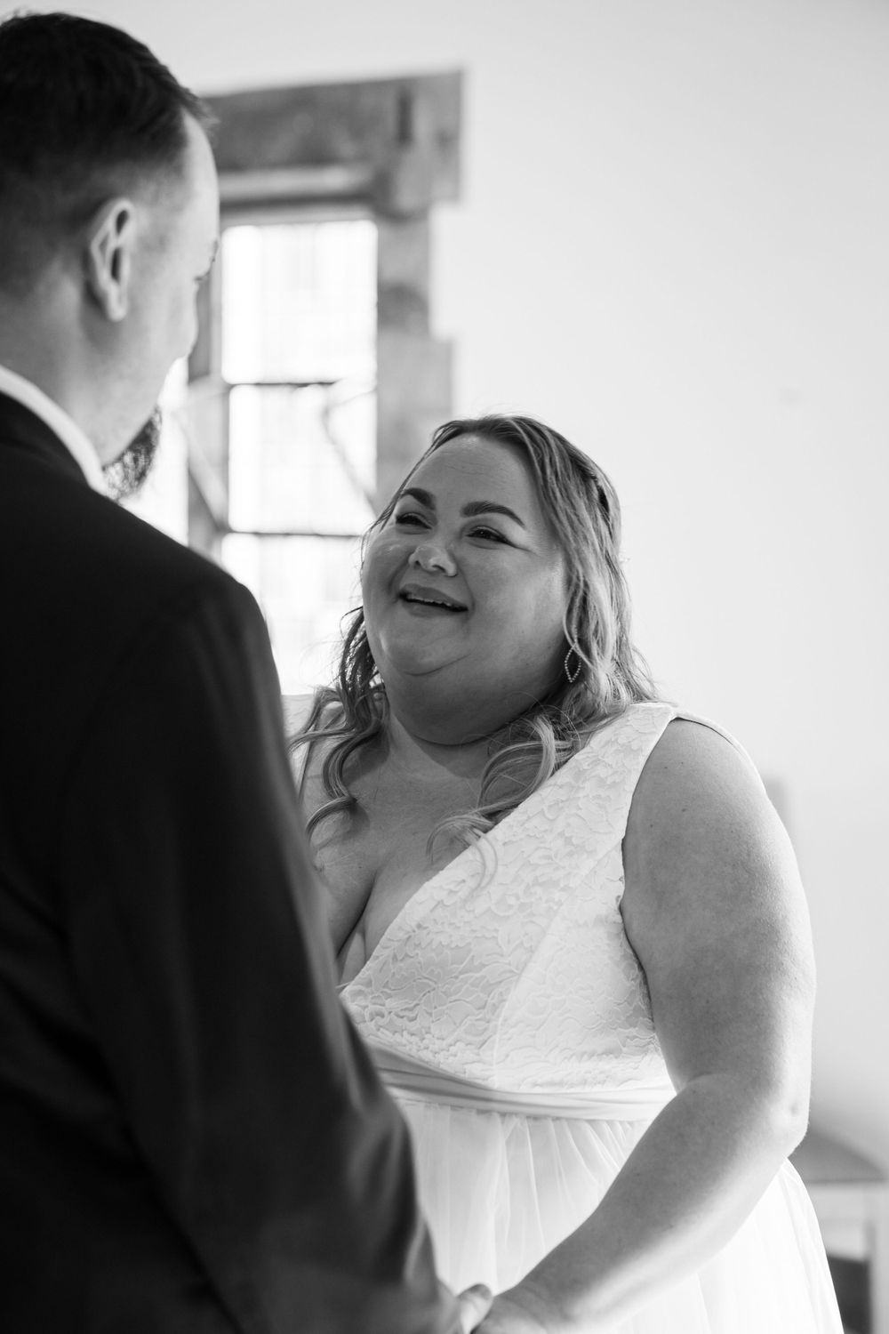 A tender moment captured in black and white as a bride in a lace wedding dress smiles joyfully during the ceremony.