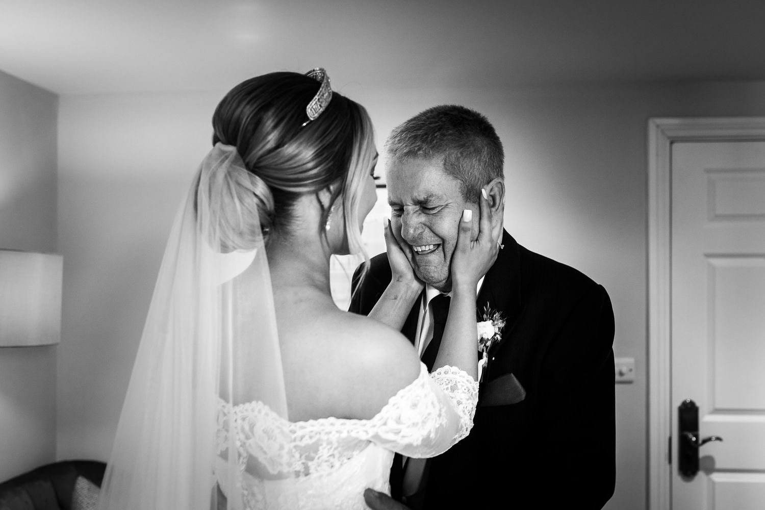 Black and white wedding photograph showing an intimate emotional moment between bride in lace dress and father of the bride