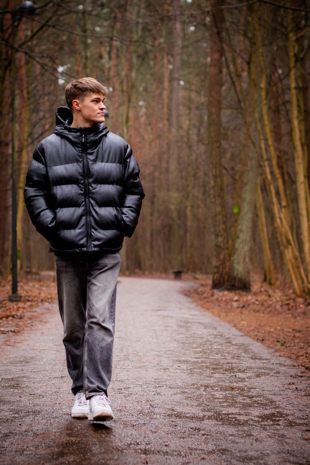 Person walking on forest path wearing puffy black jacket and grey pants.