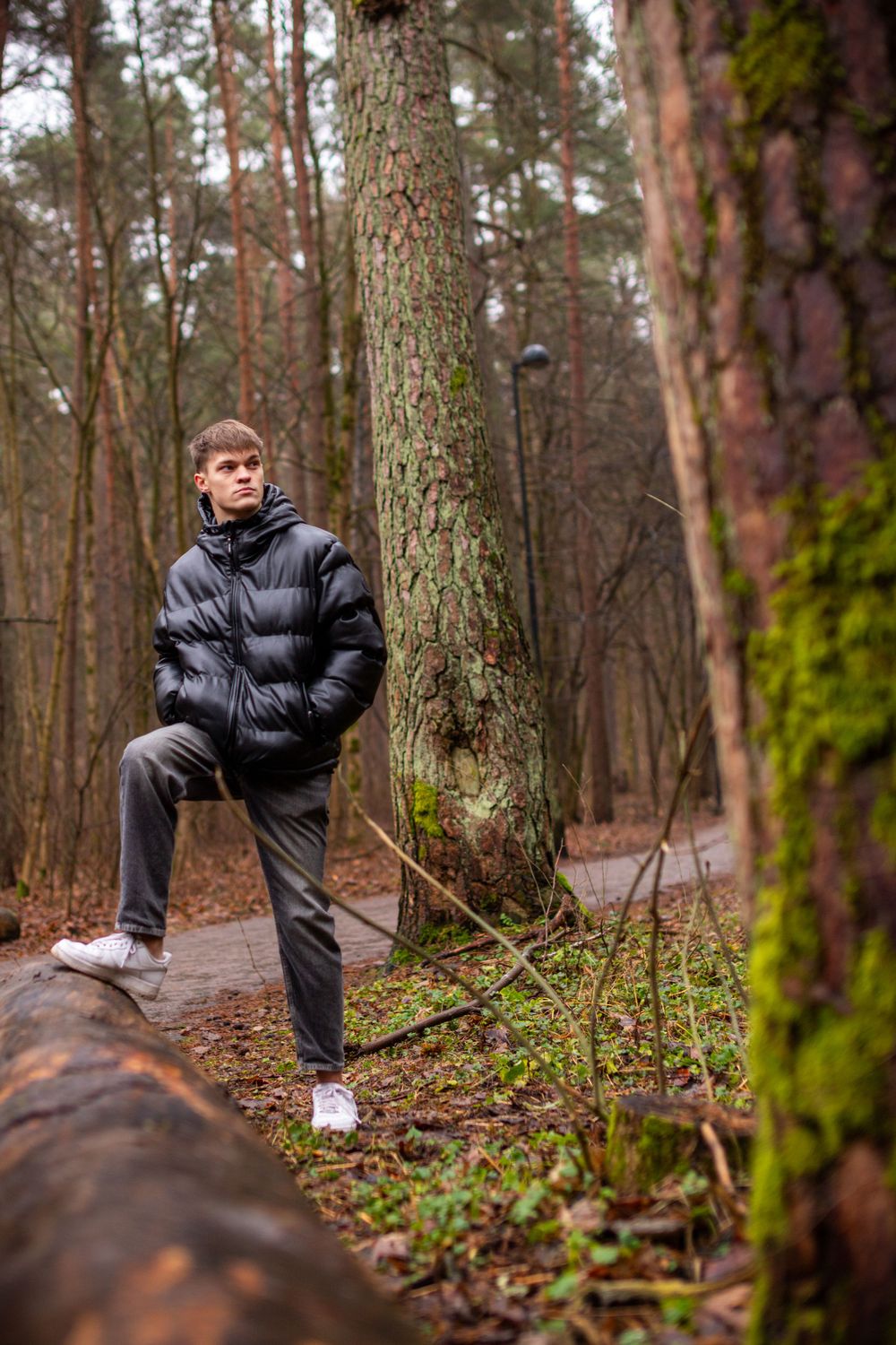 Person in black puffer jacket posing by tree trunk on woodland path.