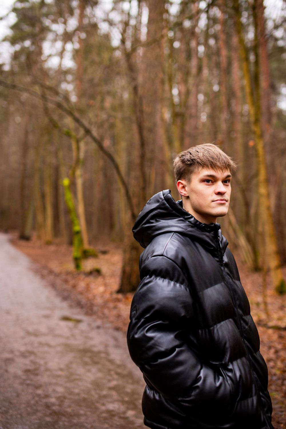 Person in black puffer jacket standing on forest path during autumn.