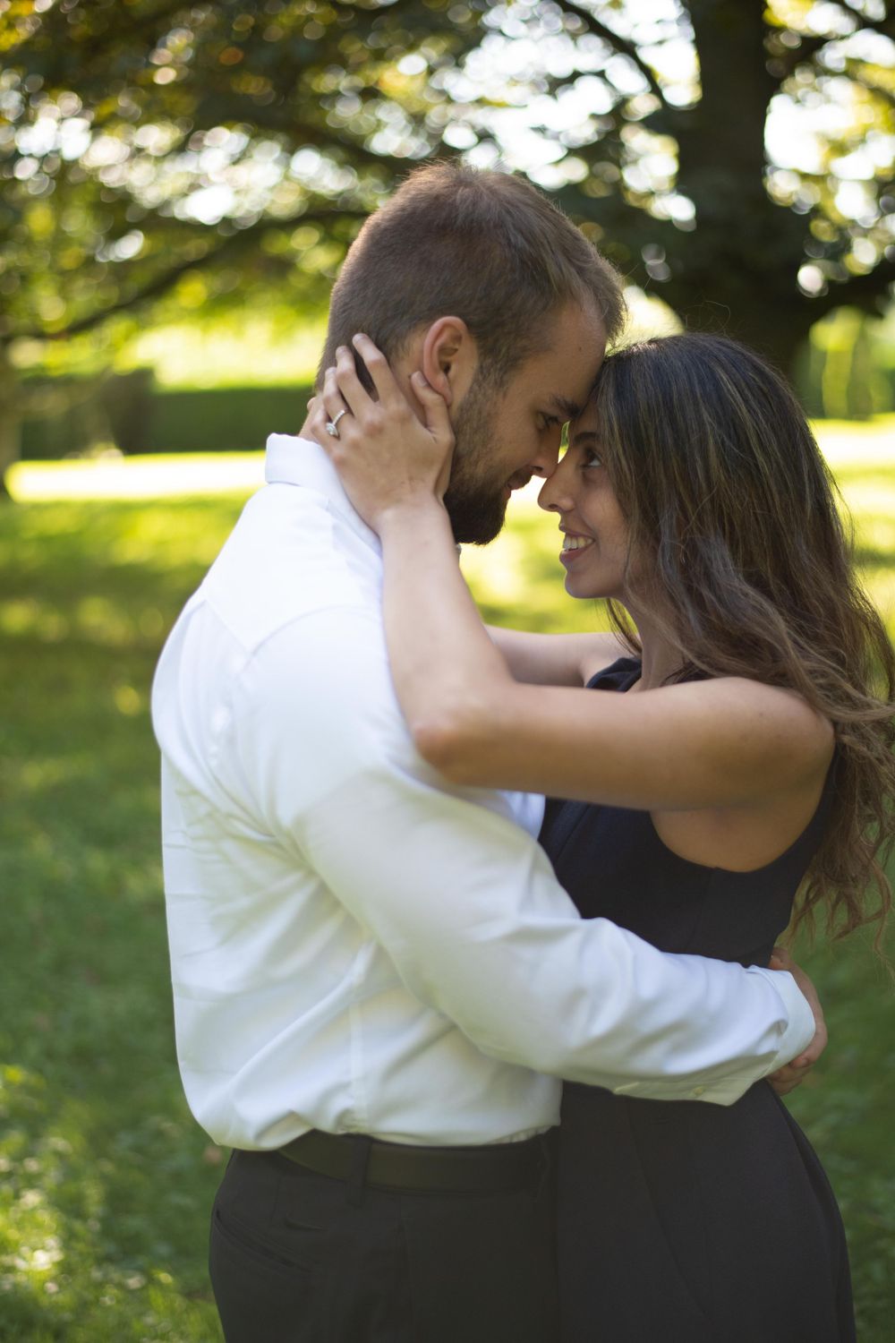 A romantic couple embracing outdoors in a sunlit garden setting with trees in the background.
