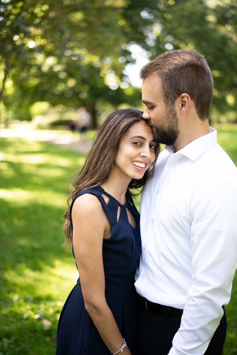 A couple shares a tender moment together in a sunny garden setting with green trees in the background.