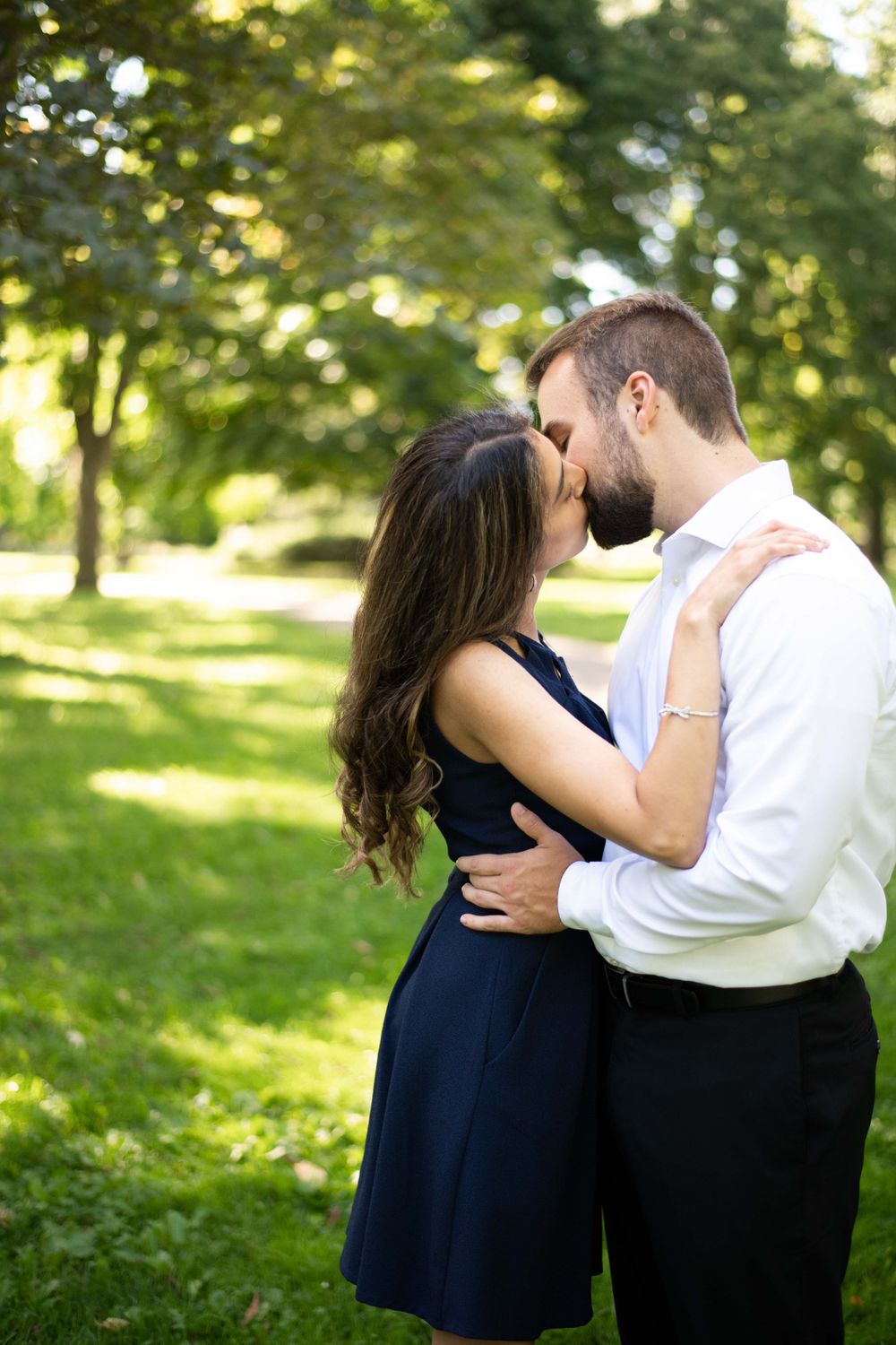 A romantic moment between a couple embracing in a sunlit park, with soft bokeh from trees in the background.