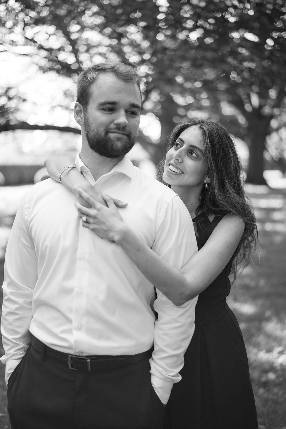 A romantic black and white portrait of a couple embracing outdoors with bokeh lighting effects.