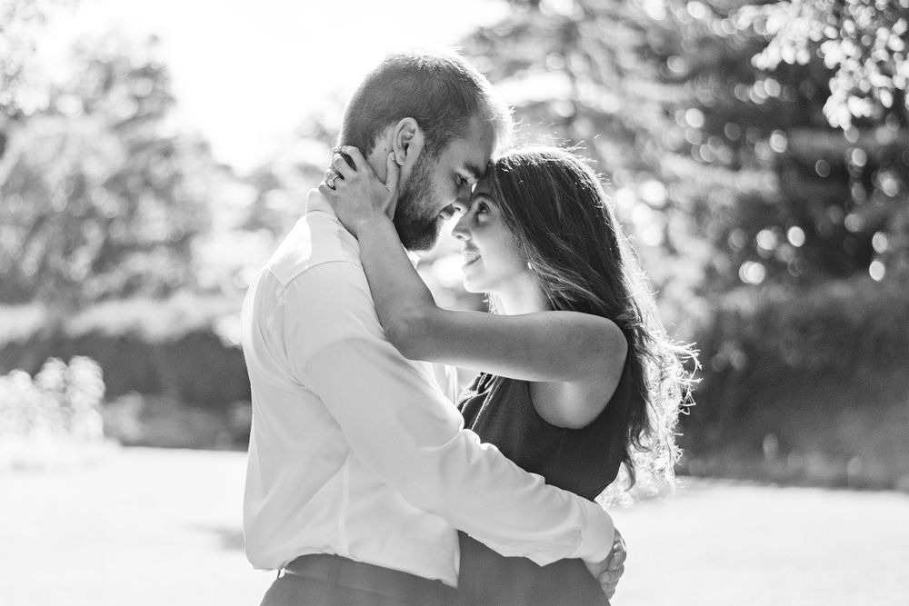A romantic black and white photo of a couple embracing outdoors in soft sunlight.