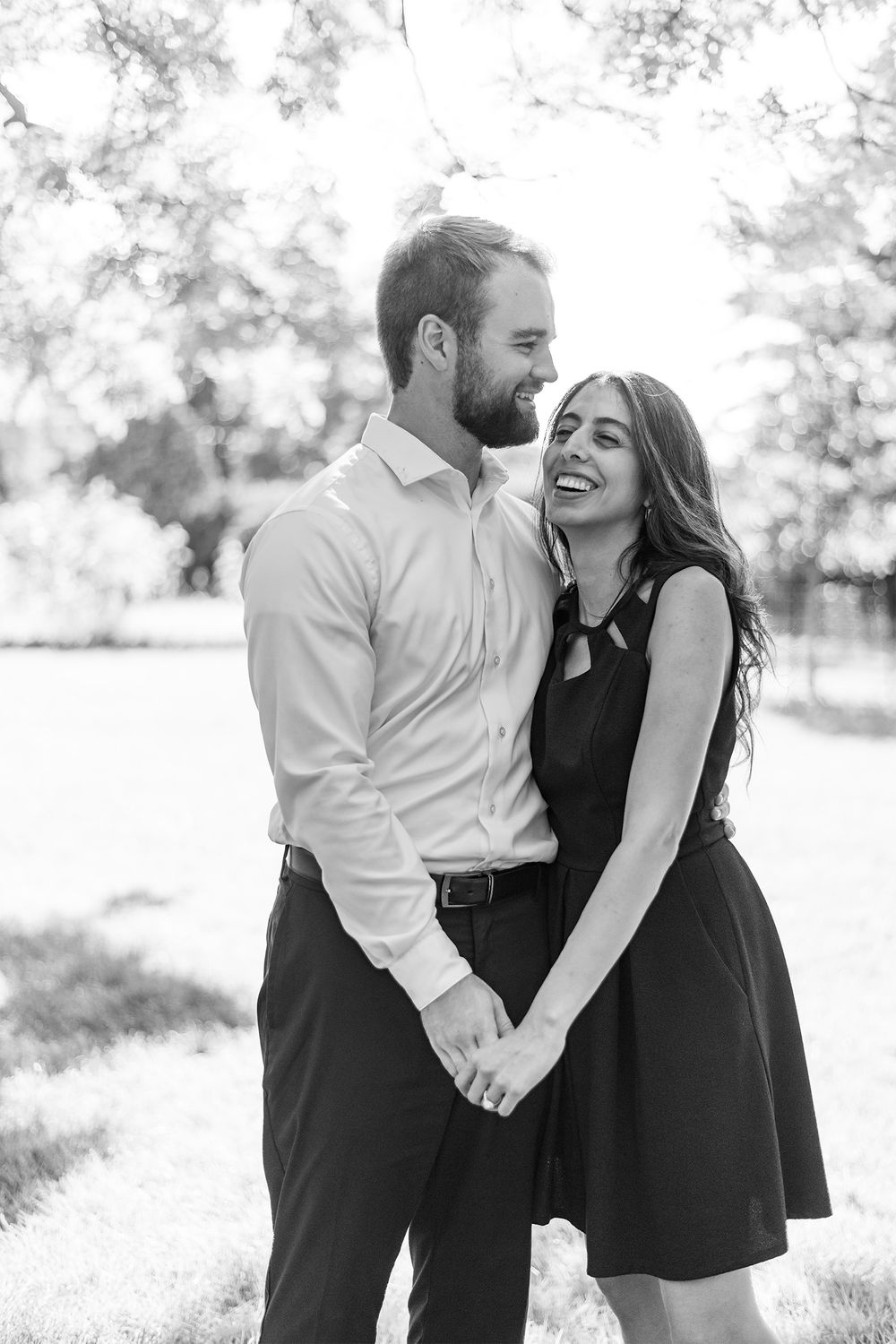 A couple shares a joyful candid moment together outdoors in black and white photography.