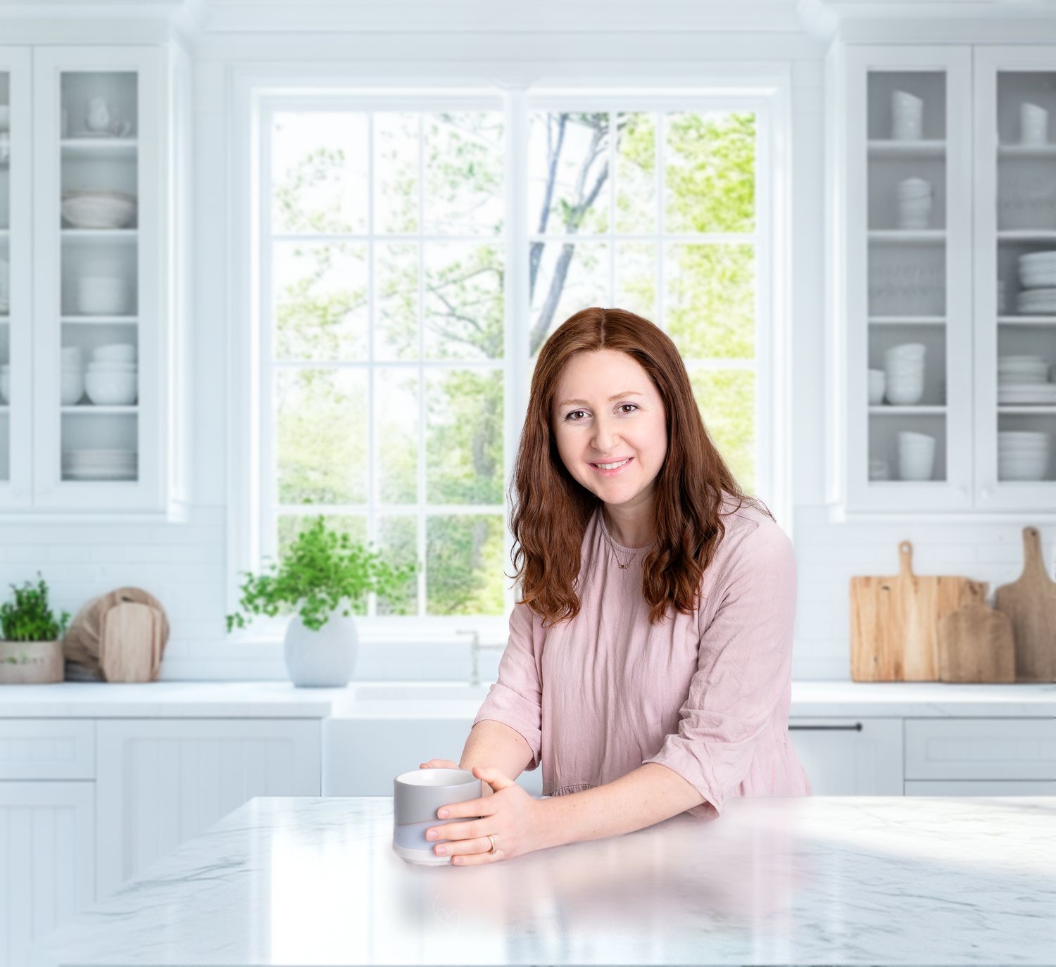 Woman relaxes with a drink in a bright modern kitchen with white cabinets and a large window. Photographed by Flora Levin Photography