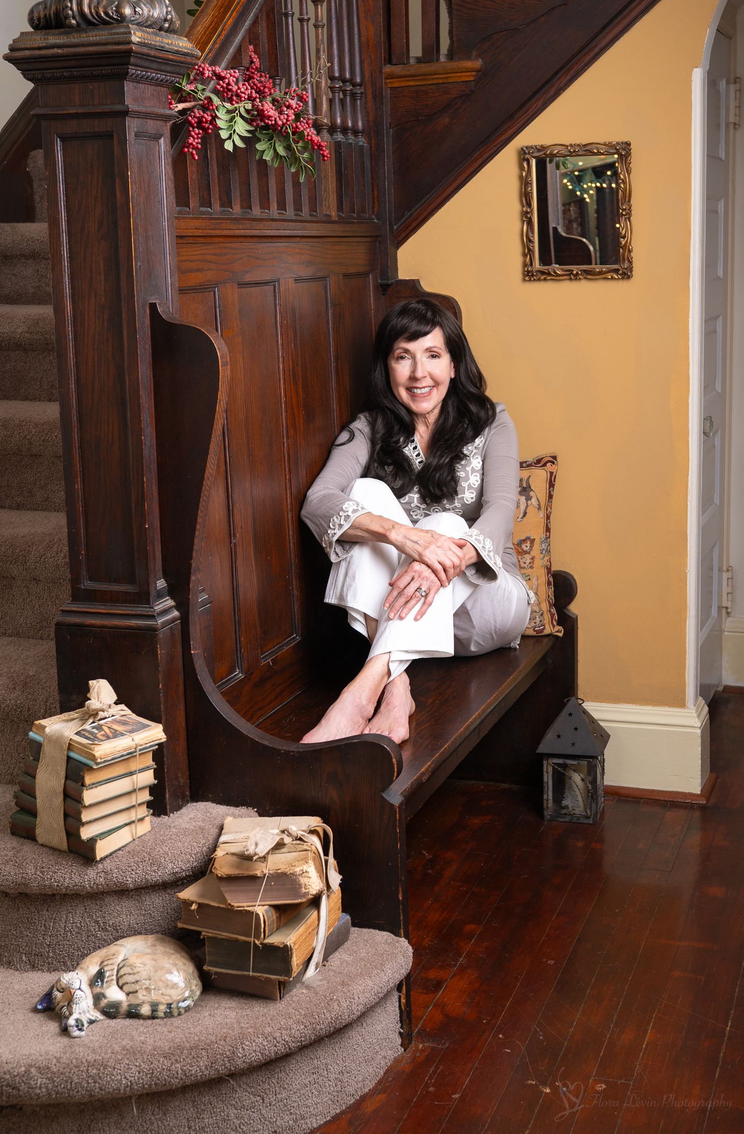 A woman sits on bench in an elegant wood-paneled hallway with vintage books and decor.