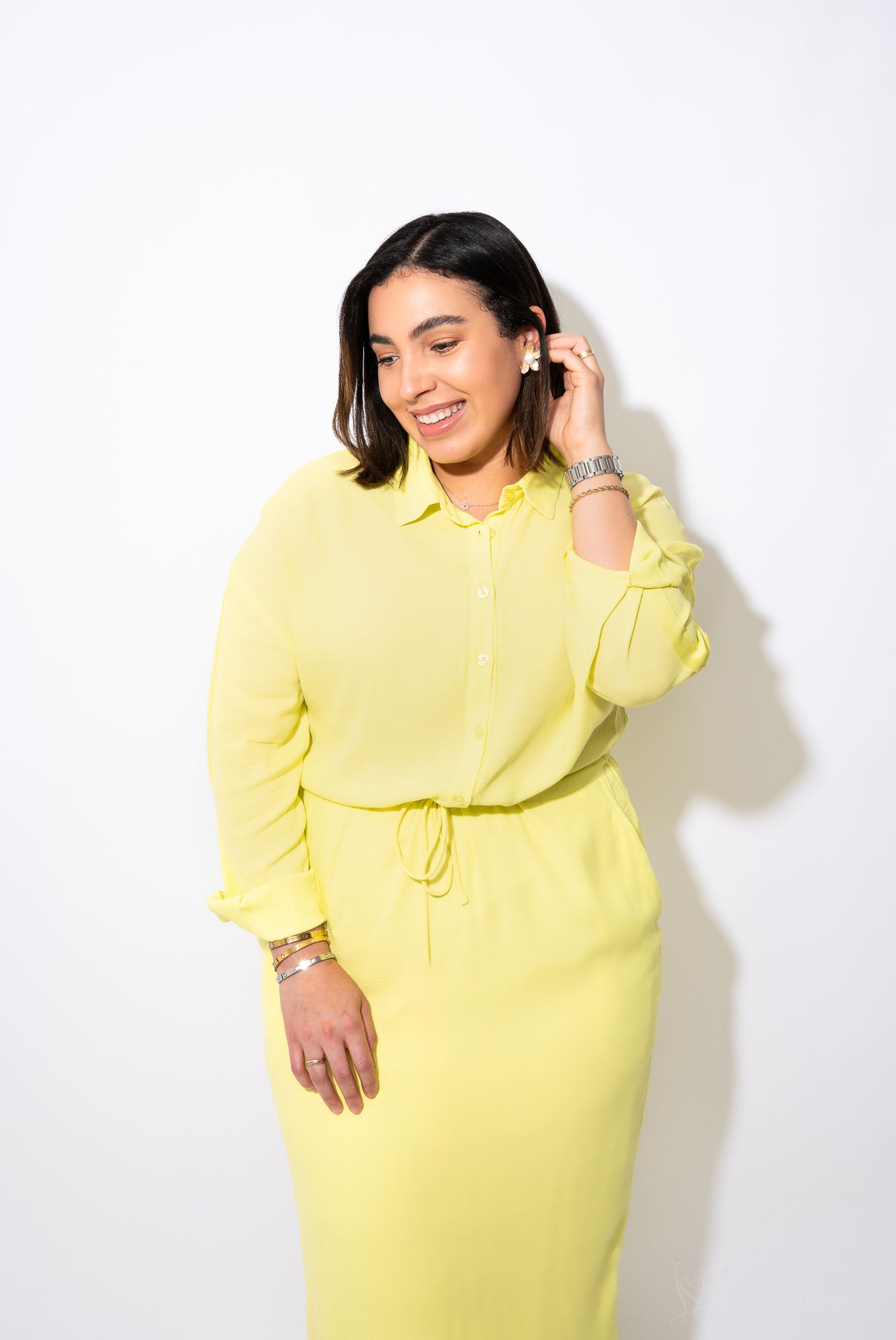 A woman wearing a bright yellow long-sleeve dress poses with a smile against a white background.