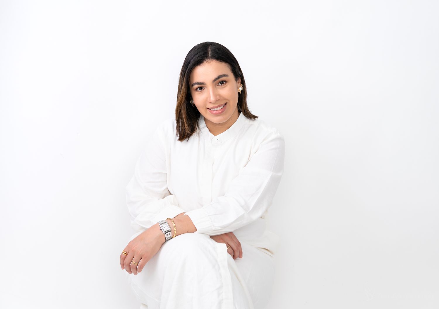A woman wearing an all-white outfit sits confidently against a white background.
