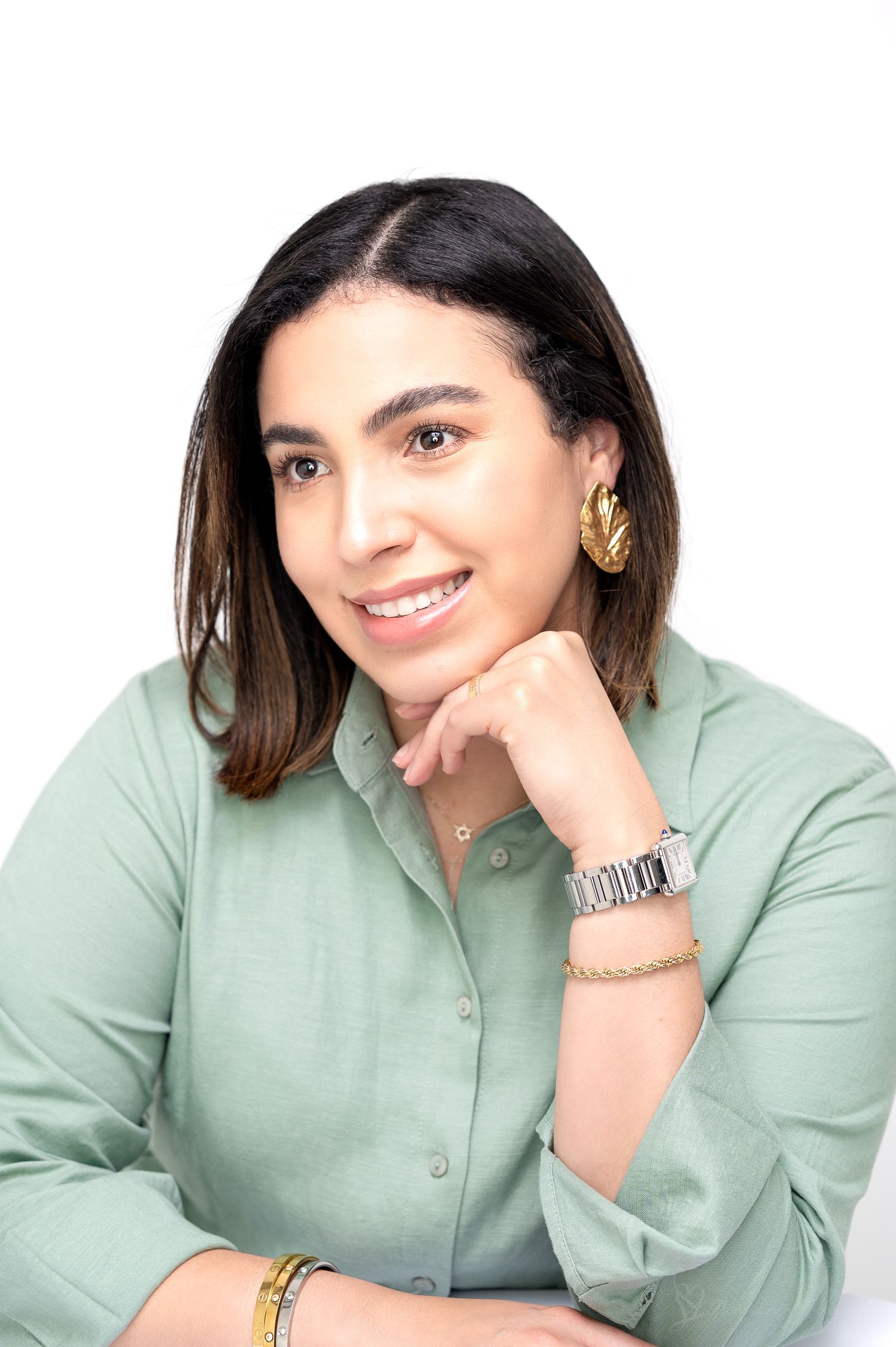 Professional portrait of a woman wearing a mint green button-down shirt and gold jewelry against white background.