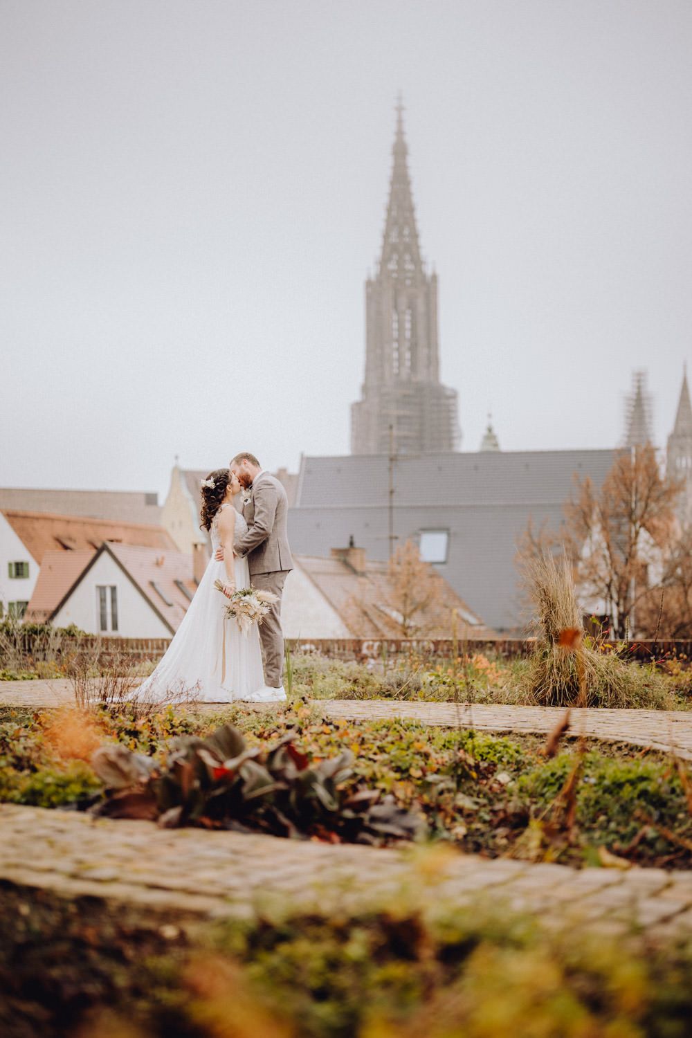 Artistic wedding photography capturing couple's embrace with gothic architecture and autumn gardens.