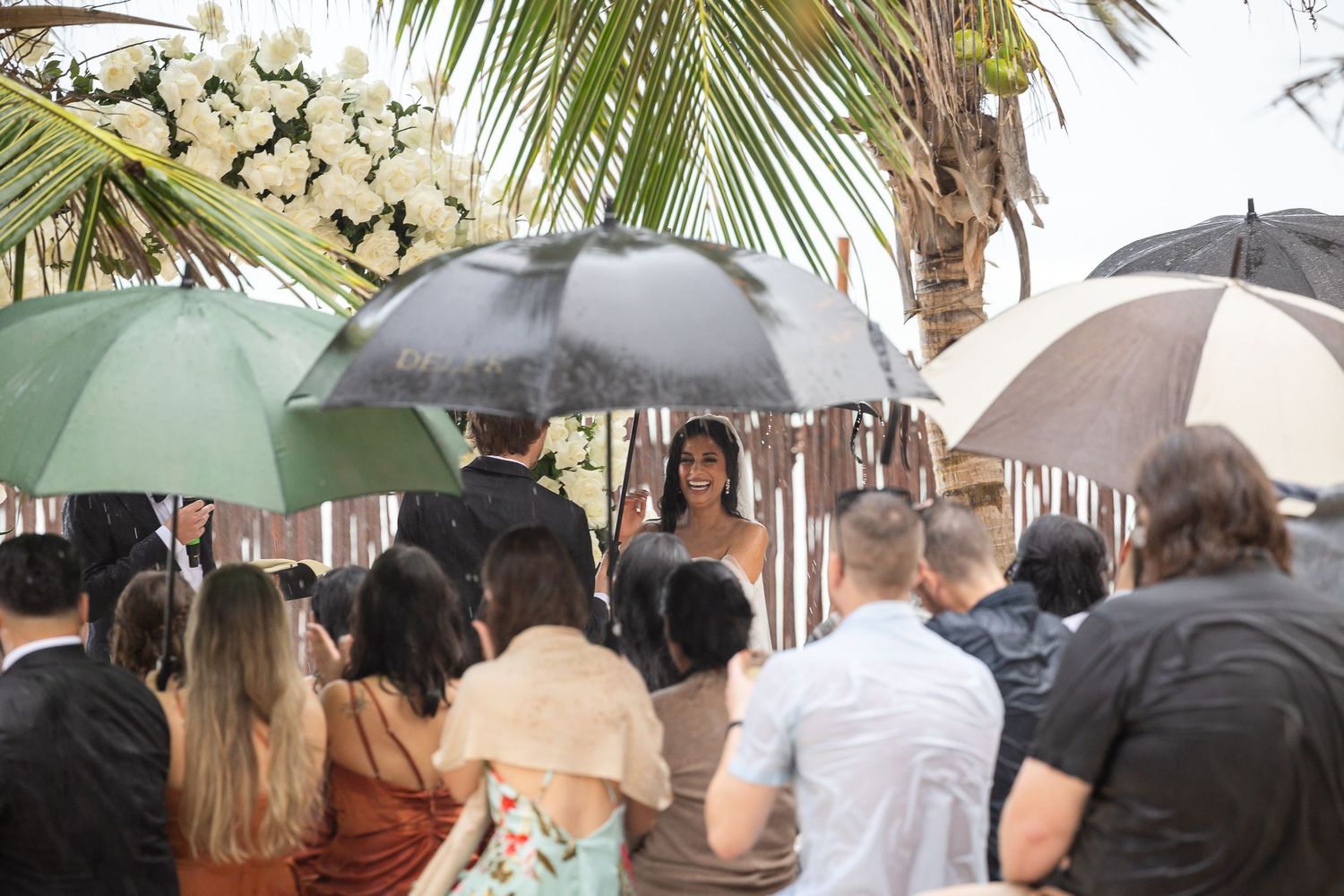 Wedding ceremony under umbrellas at a tropical destination with palm trees.