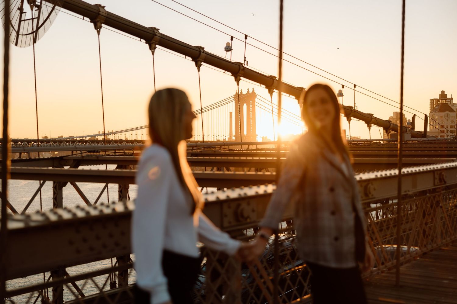 A couple holds hands on a bridge with the sun setting behind them, casting a golden glow over a romantic and peaceful moment.