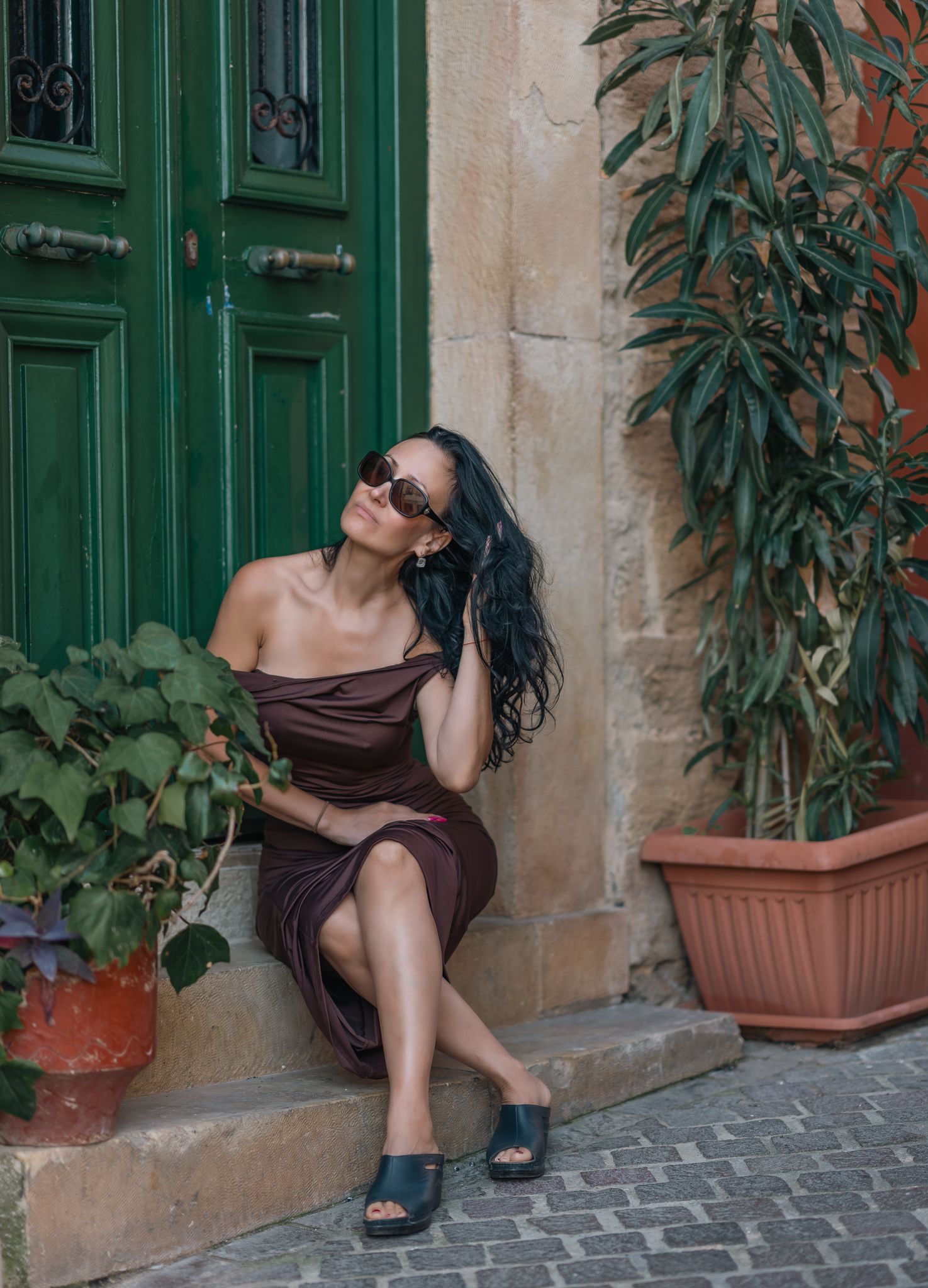 Beautyfotografie - Casual portrait of woman in brown dress sitting by green door with plants.