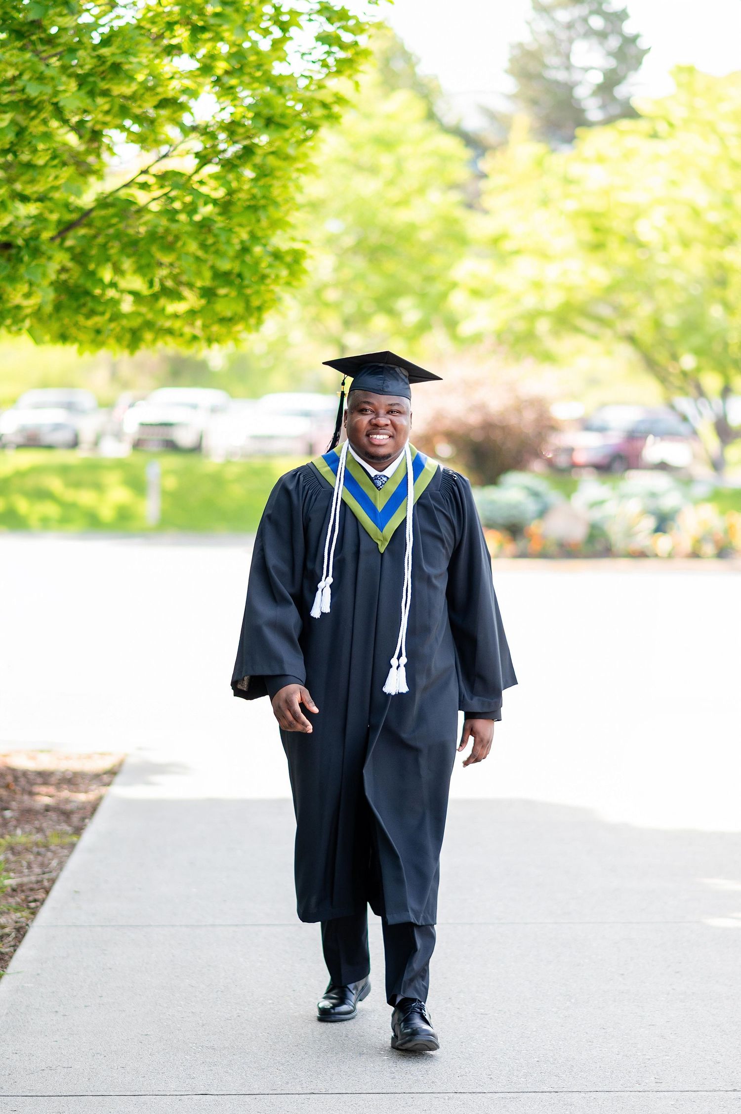 Graduate walking on campus pathway wearing black graduation gown with blue and gold stole.