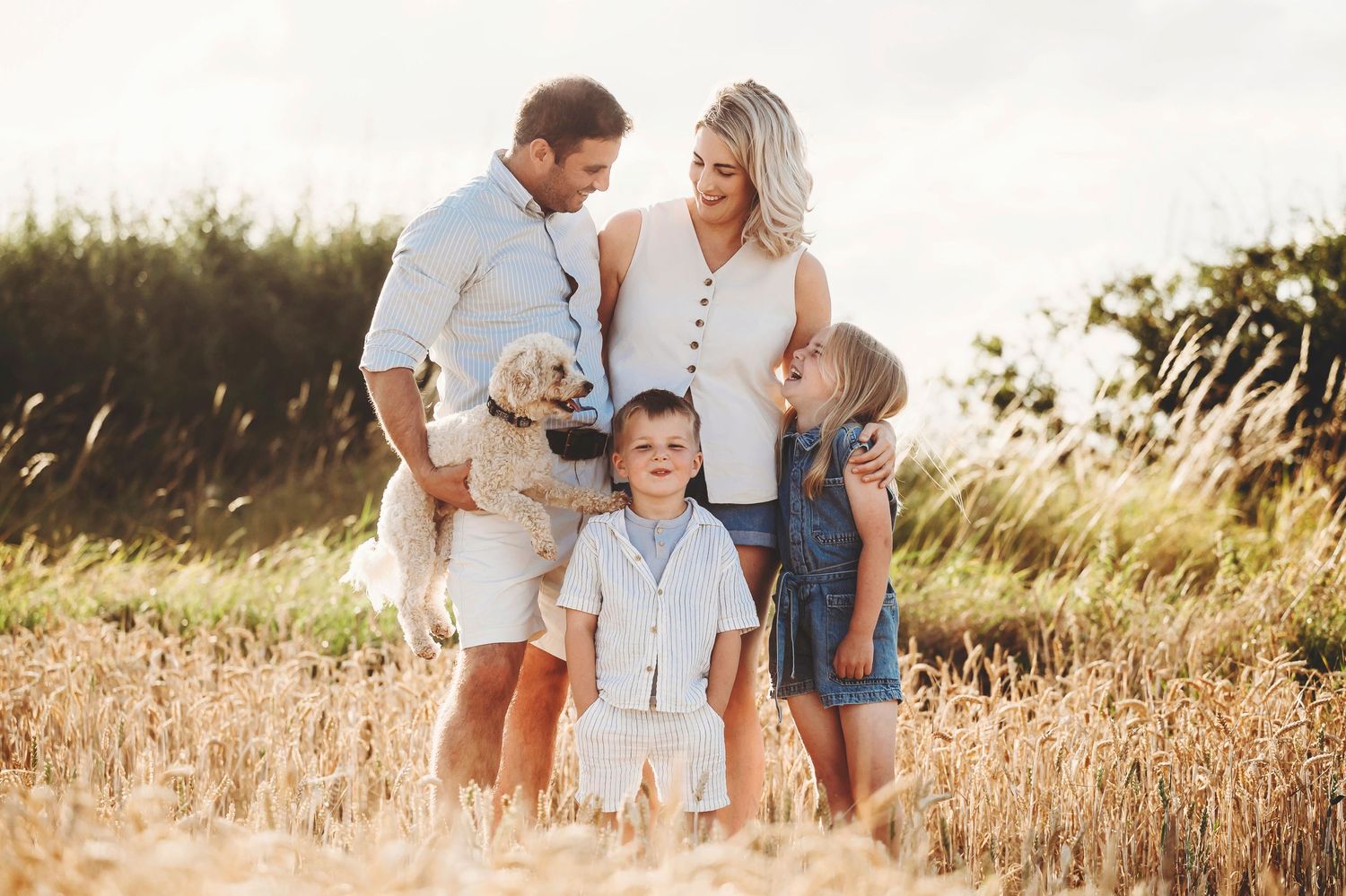 Family shares tender moment together in golden summer field during sunset photoshoot.