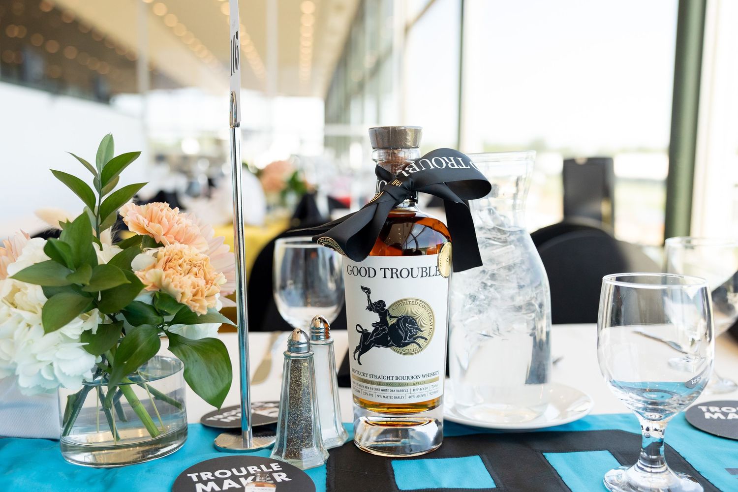 Good Trouble whiskey bottle displayed on a decorated event table with flowers and glassware.