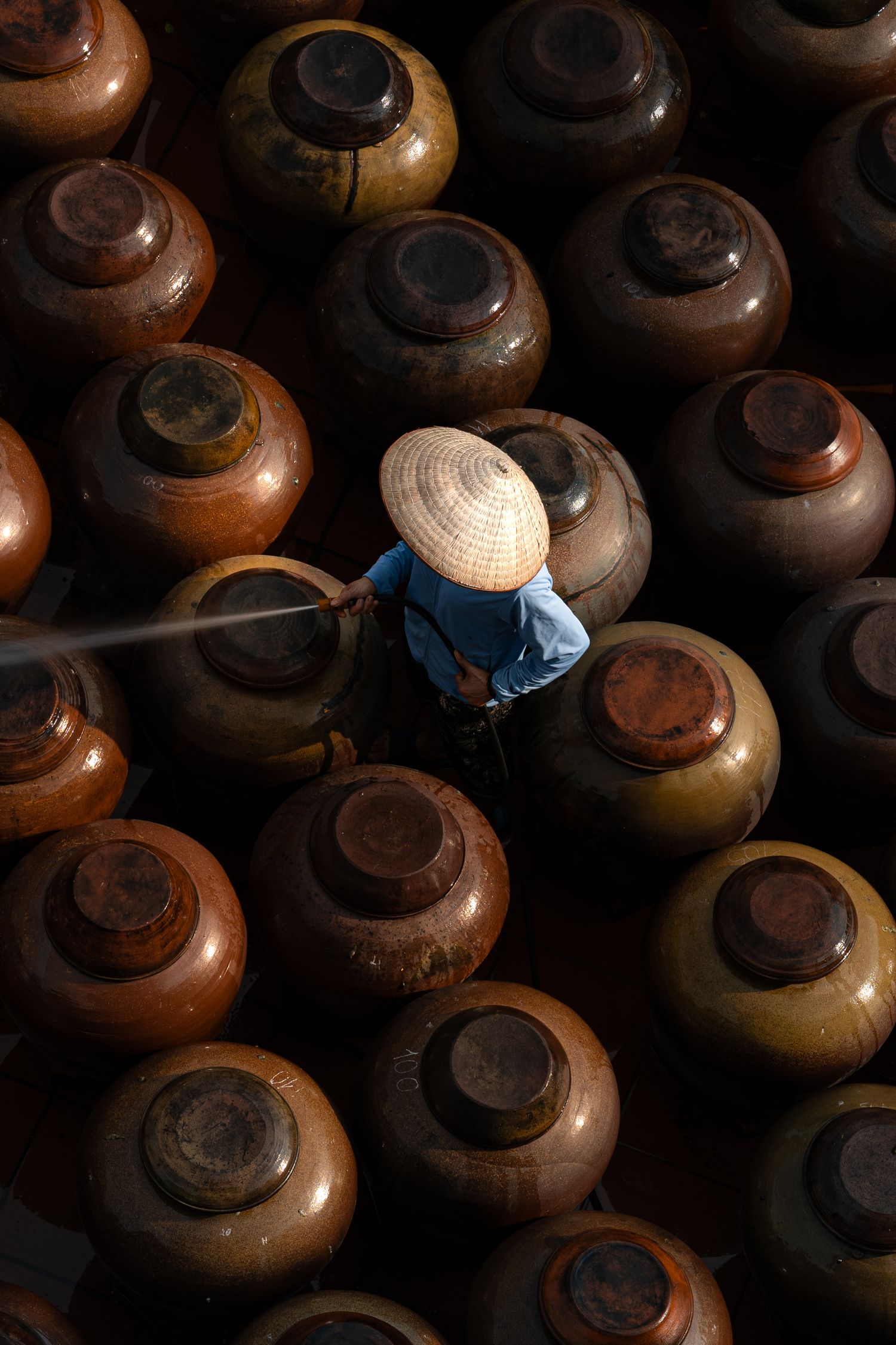 Clay pots arranged in rows with light filtering through gaps creating an atmospheric pattern.