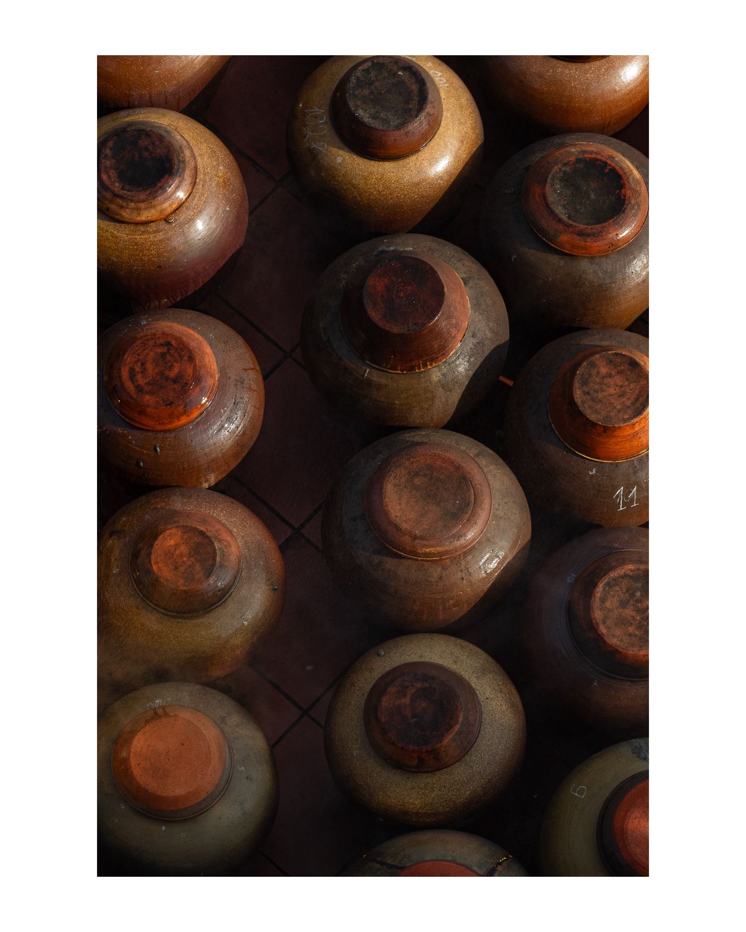 Traditional clay pots arranged in rows on a dark background creating a dramatic lighting pattern.