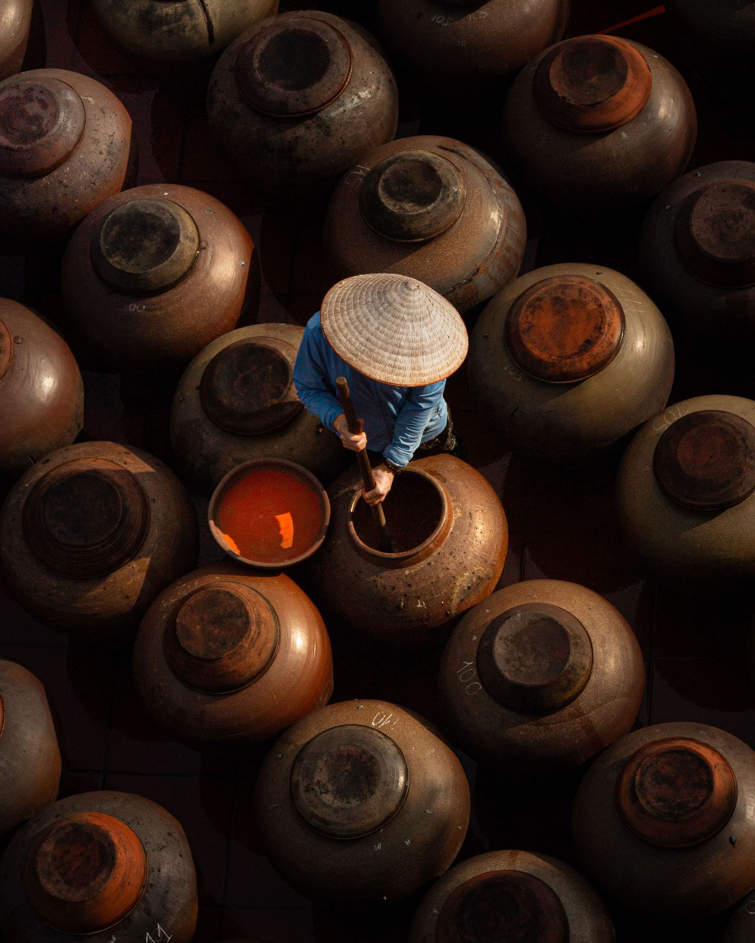Rustic clay vessels arranged in rows with warm light glowing through openings.