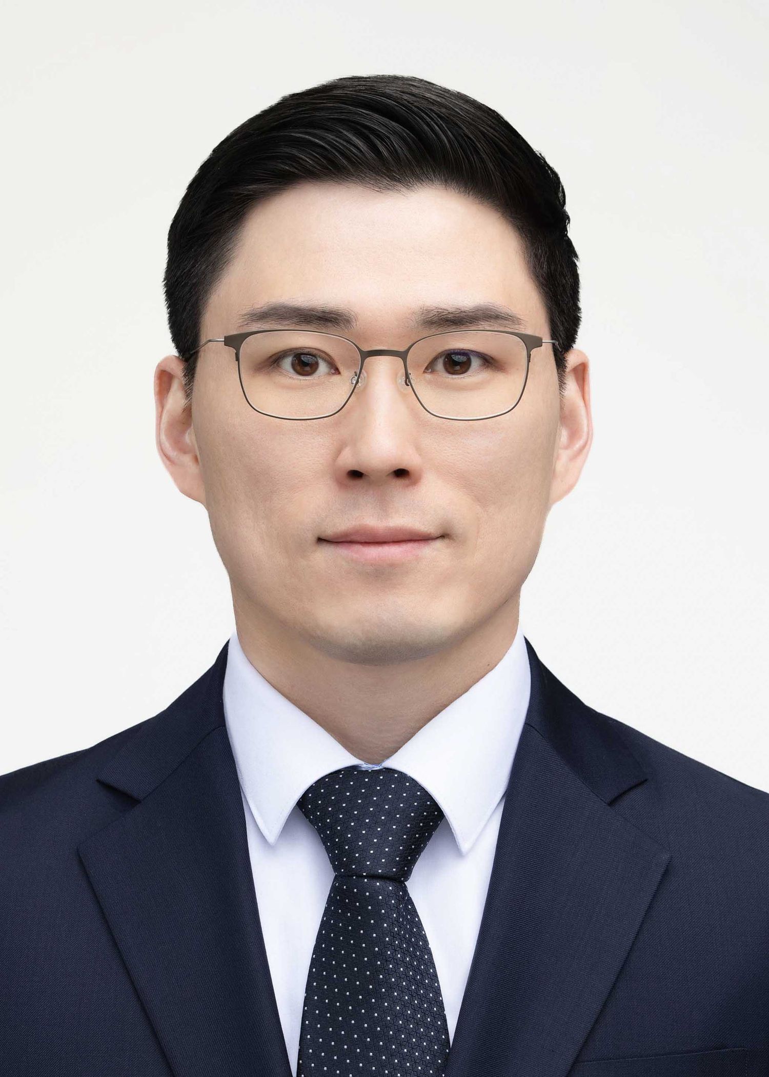Passport and ID portrait of a man wearing glasses and a navy suit against a white background.