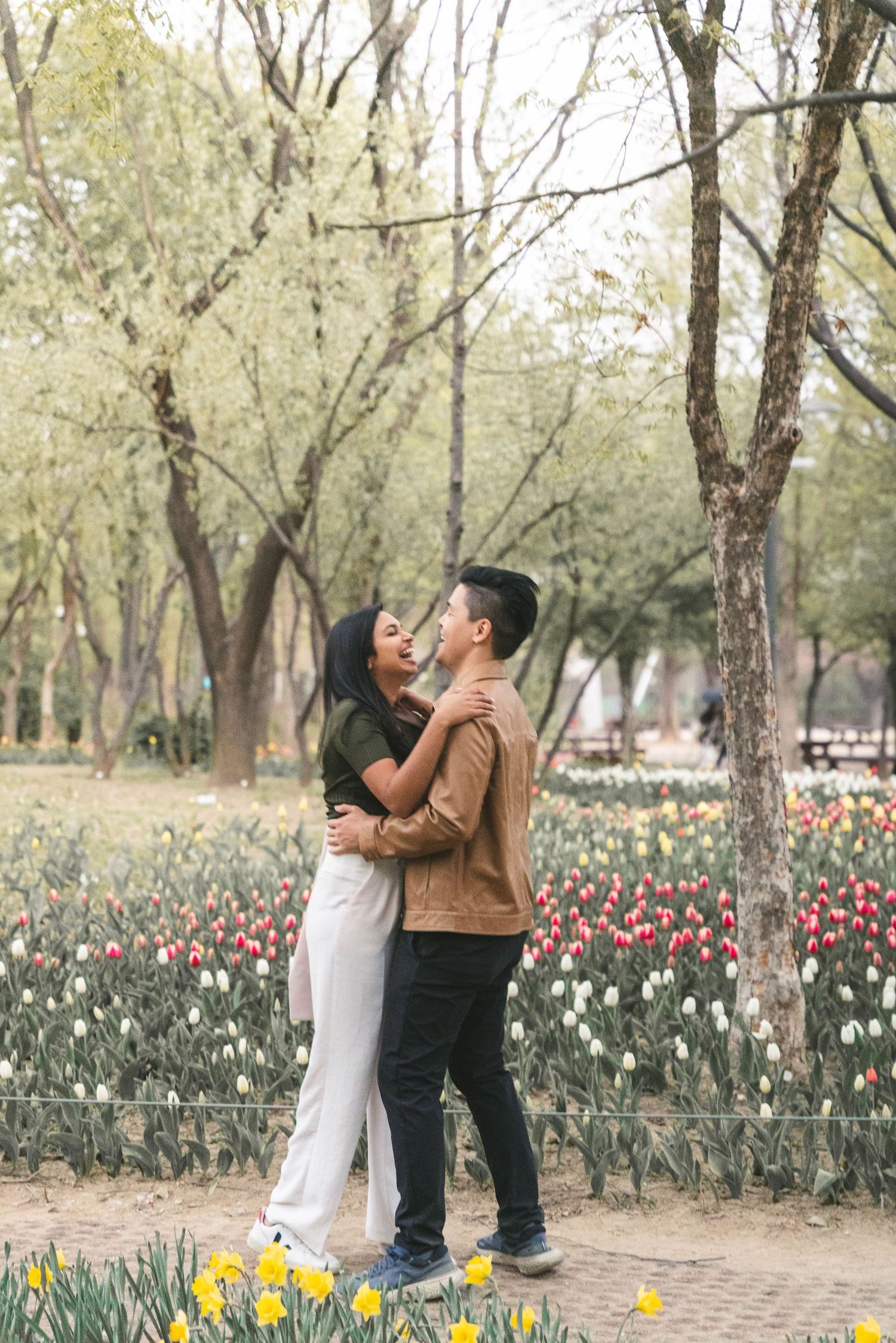 A romantic couple embraces in a spring garden filled with blooming tulips and daffodils on a serene path.