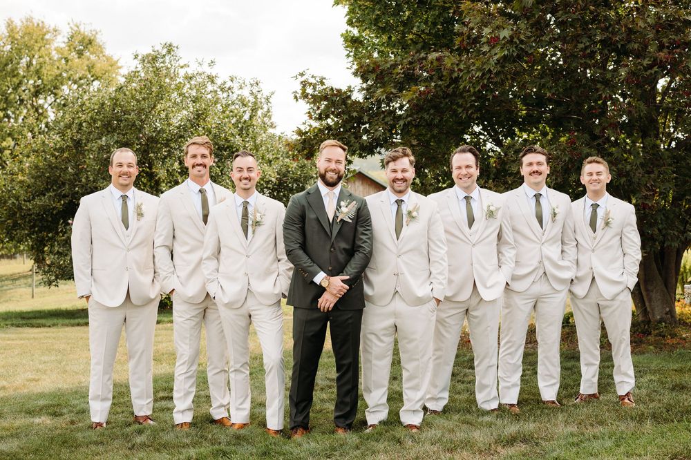 Wedding party of groomsmen in matching white suits posing together outdoors.