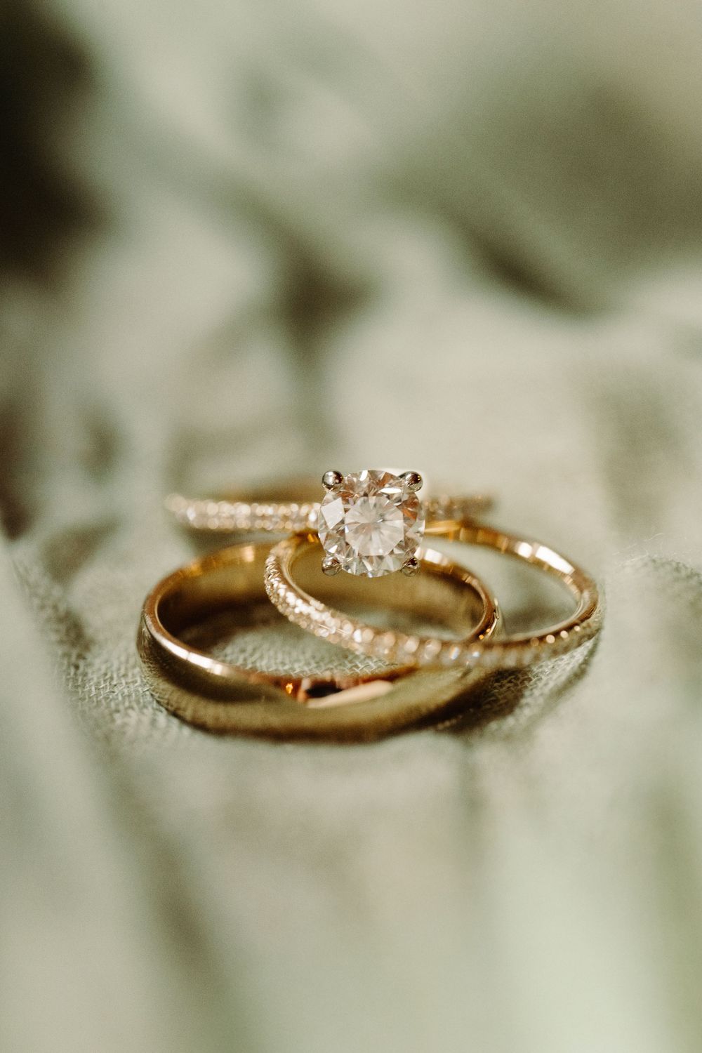 Three elegant wedding rings including a diamond engagement ring and matching bands rest on a soft fabric surface.