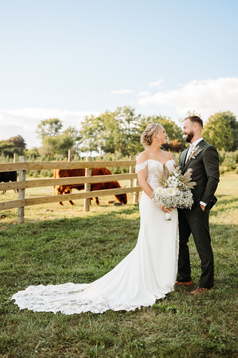 A newlywed couple shares intimate moments in a sunlit field with white floral details and a flowing wedding dress.