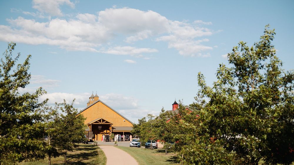 Panoramic view of a rustic barn venue set against a blue summer sky with white clouds.